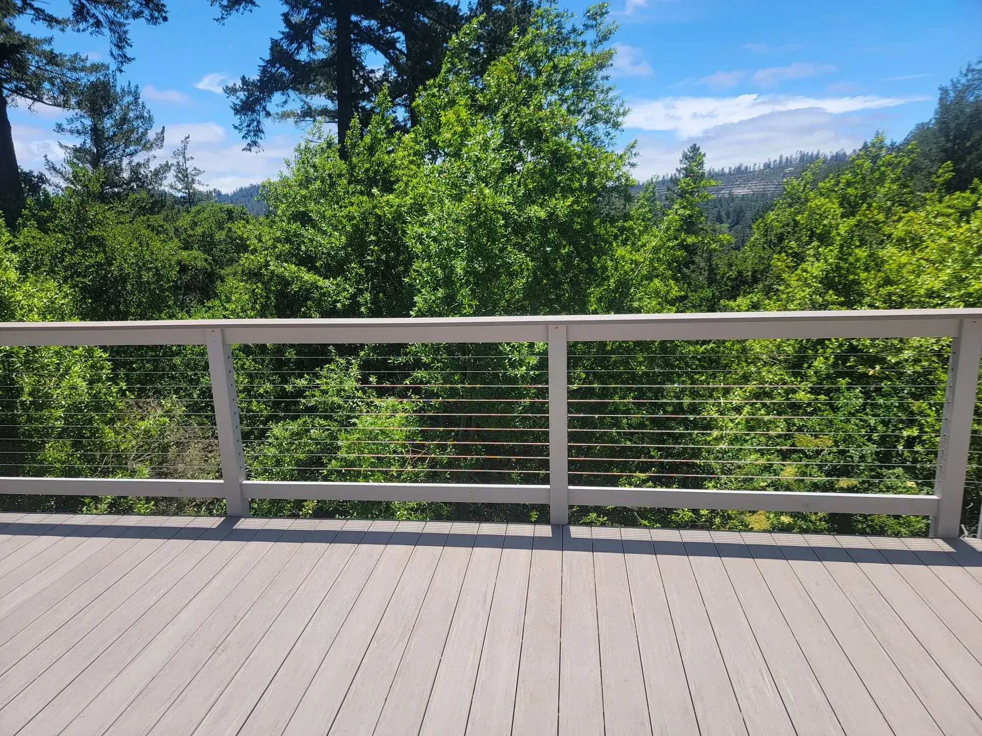 Wooden deck railing overlooking lush green trees under a blue sky