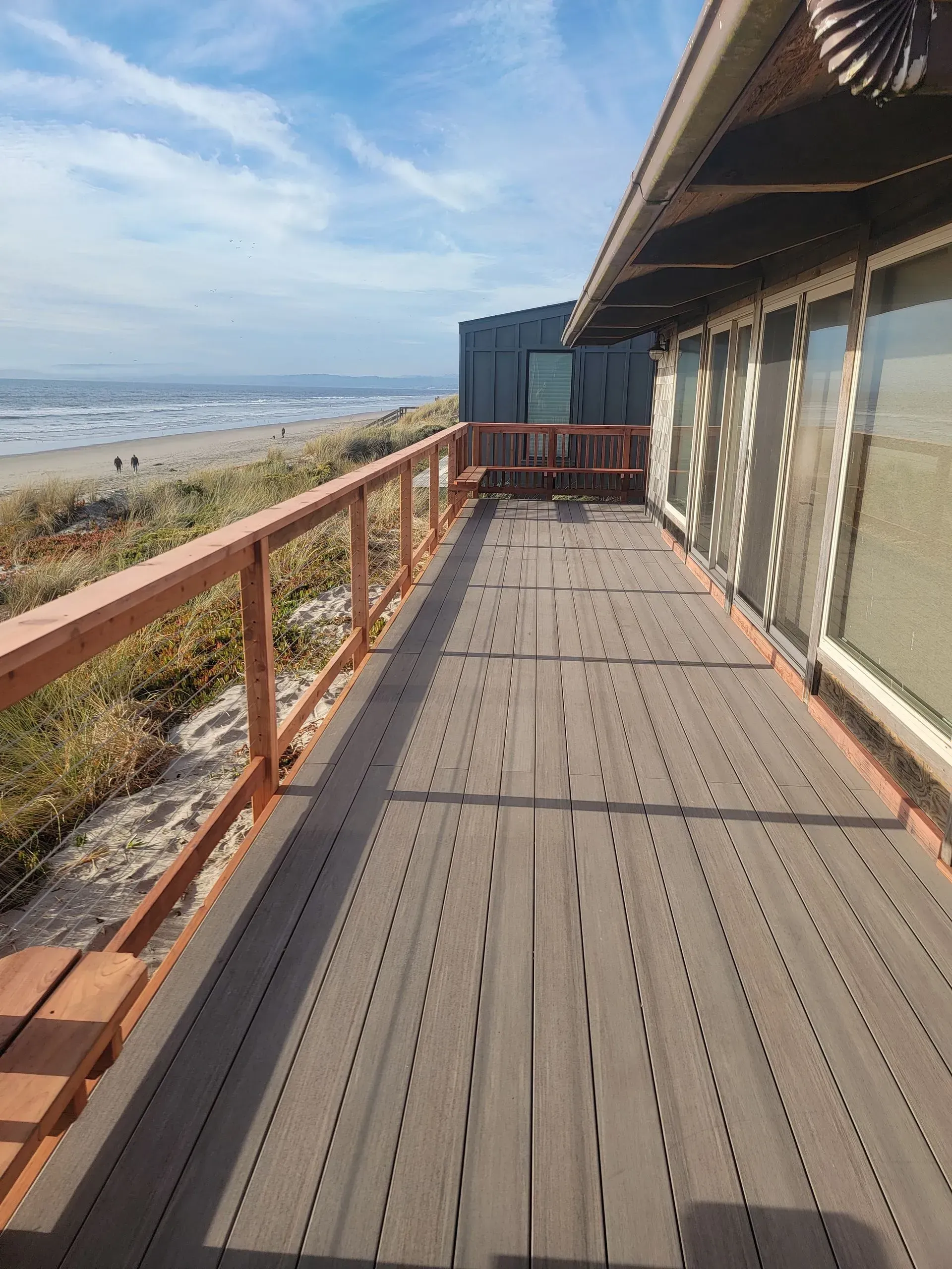 Wooden boardwalk along a beach with ocean view and building on the right.
