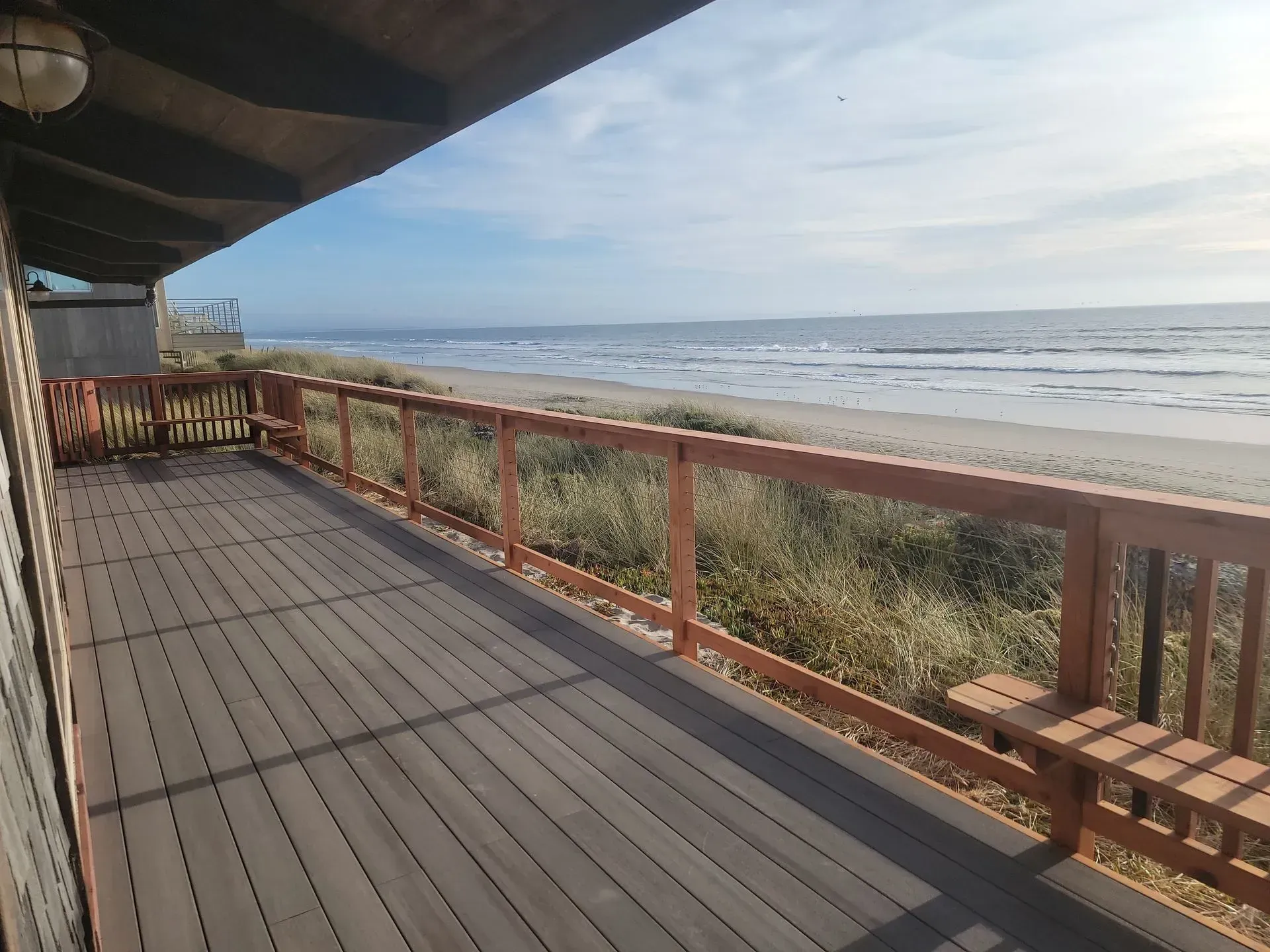Beachfront wooden deck with railing overlooking ocean waves and sand dunes