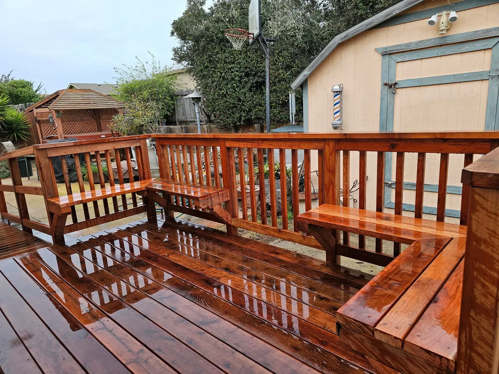 Wet wooden deck with red railing beside a beige house after rain