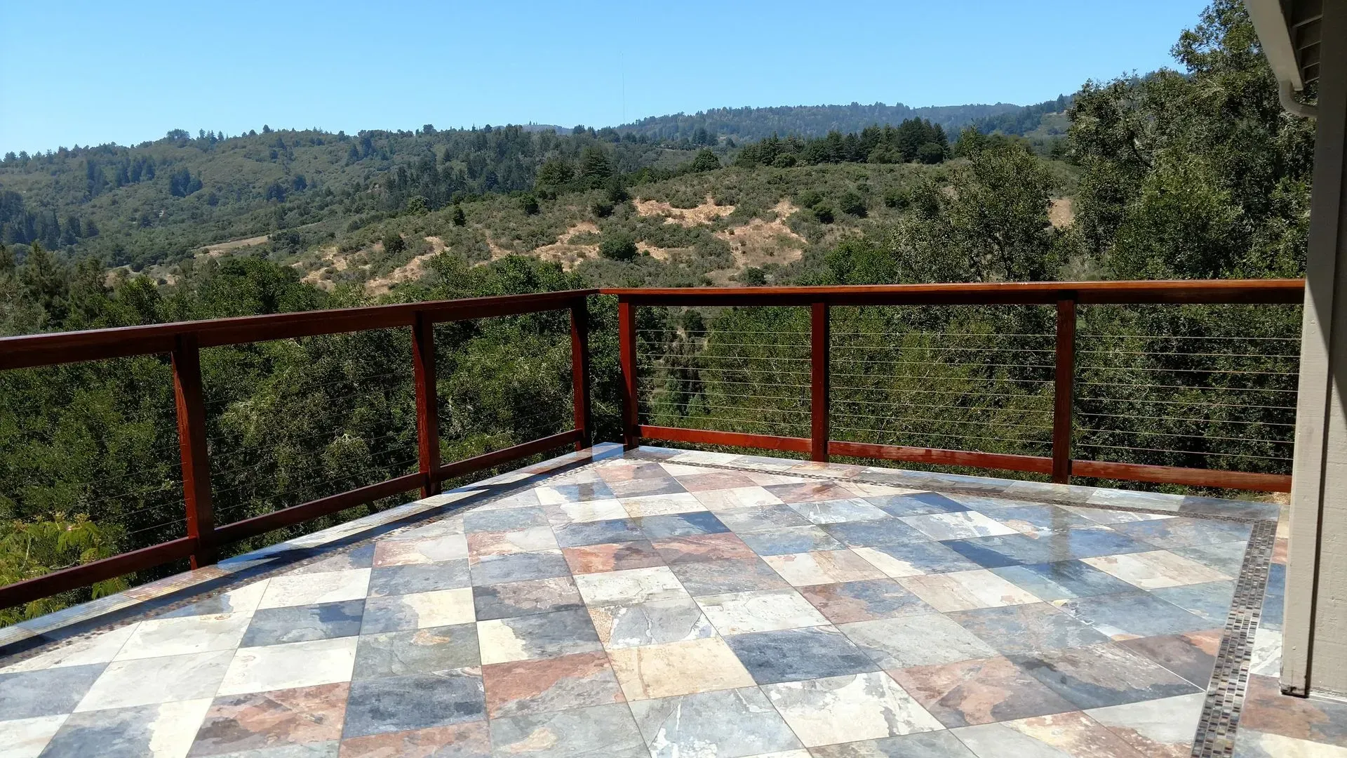 Stone terrace with red railing overlooking a forested hillside under a clear sky