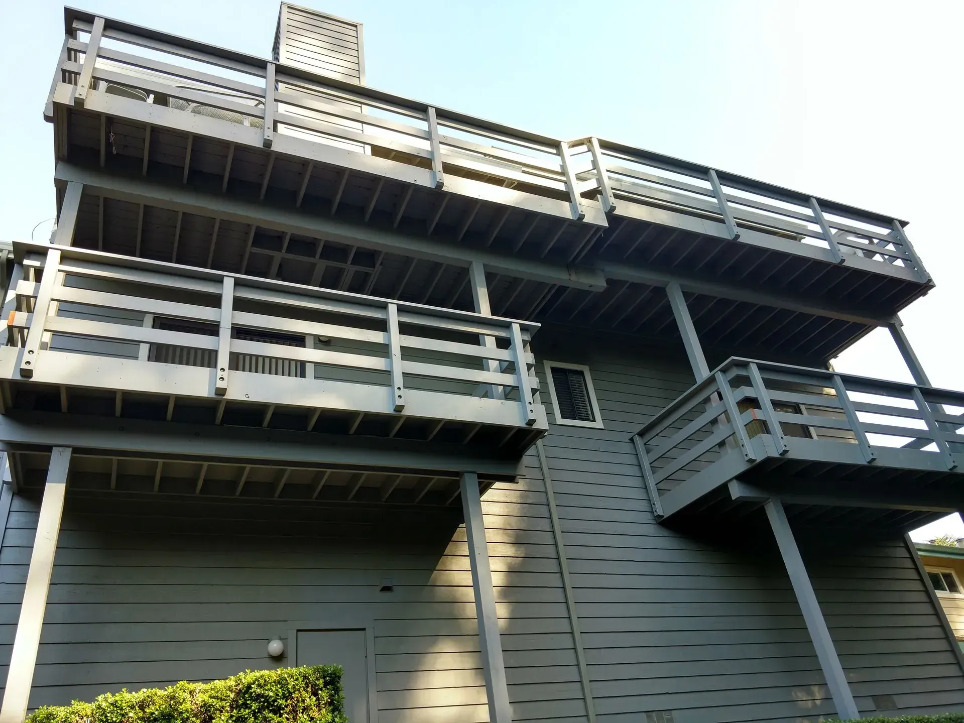 Multi-level wooden house with stacked balconies and railings under a clear sky