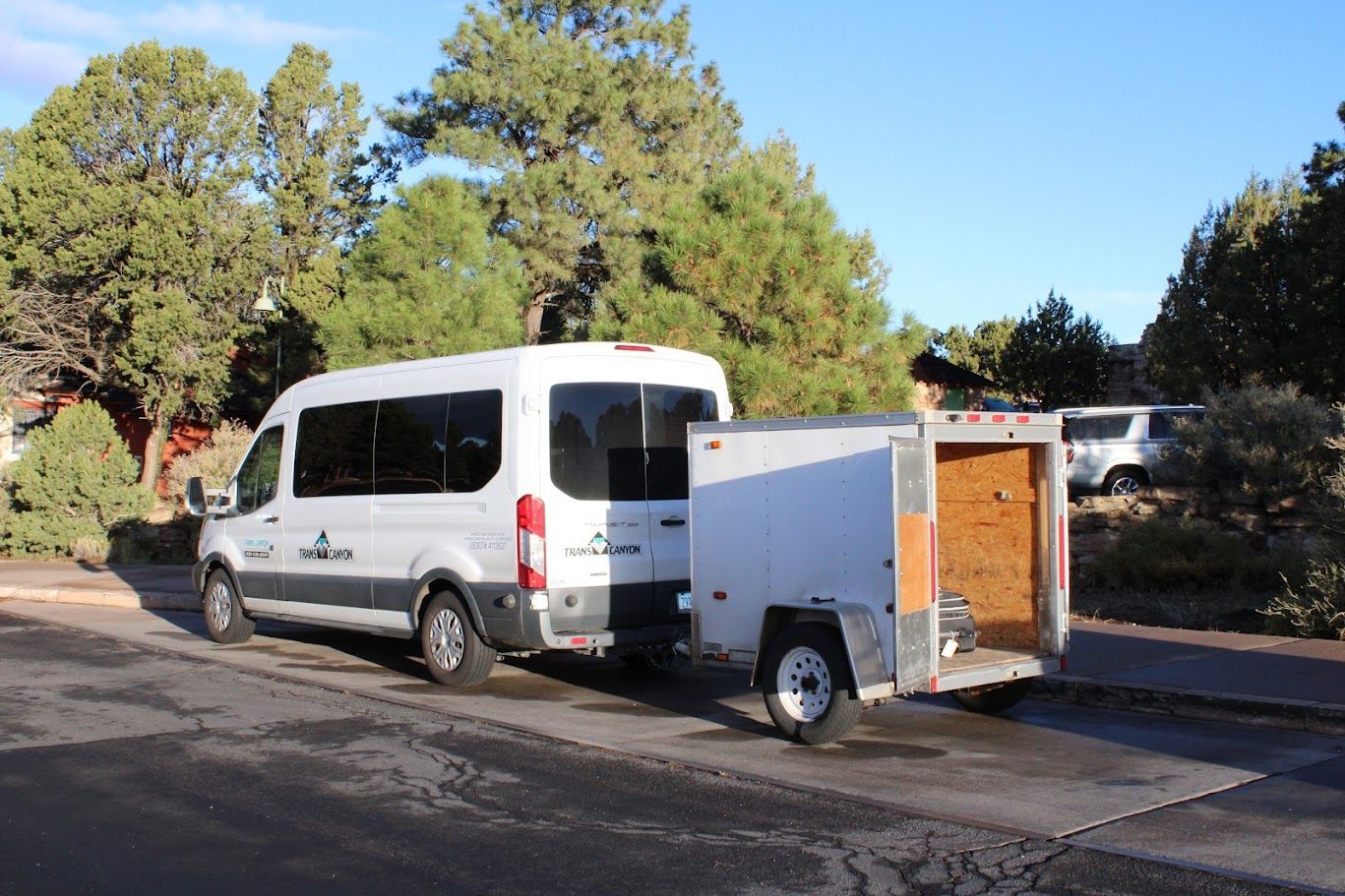 A white van with a trailer attached to it is parked on the side of the road.