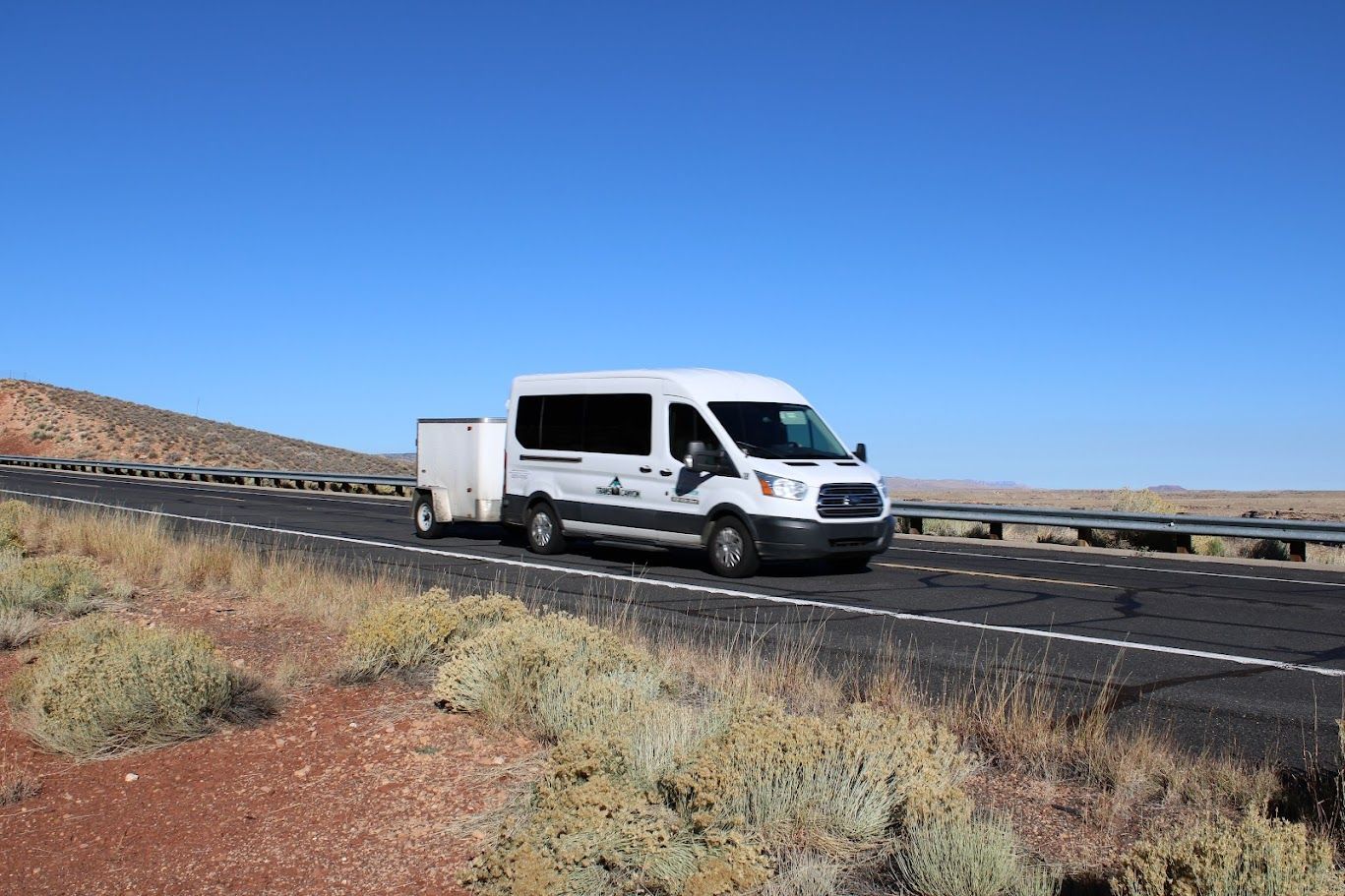 A white van is driving down a road with a trailer attached to it.