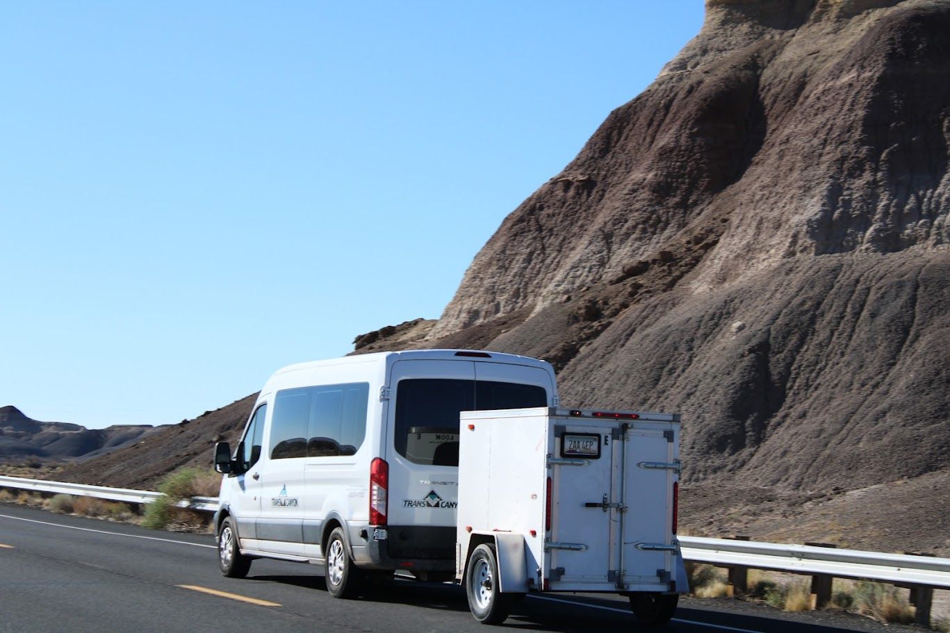 A white van with a trailer attached to it is driving down a road.