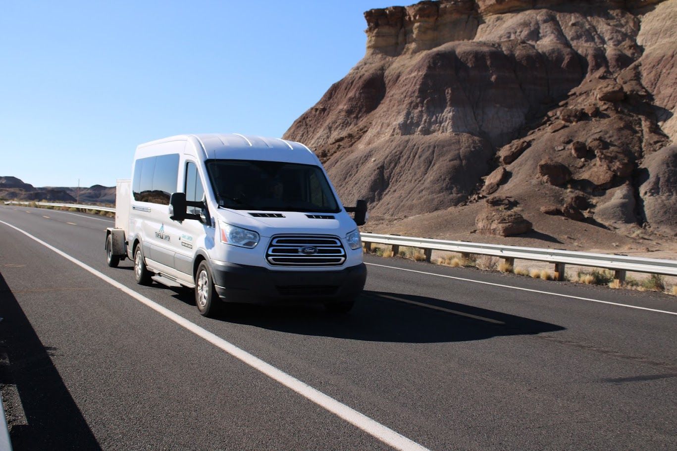 A white van is driving down a highway next to a mountain.
