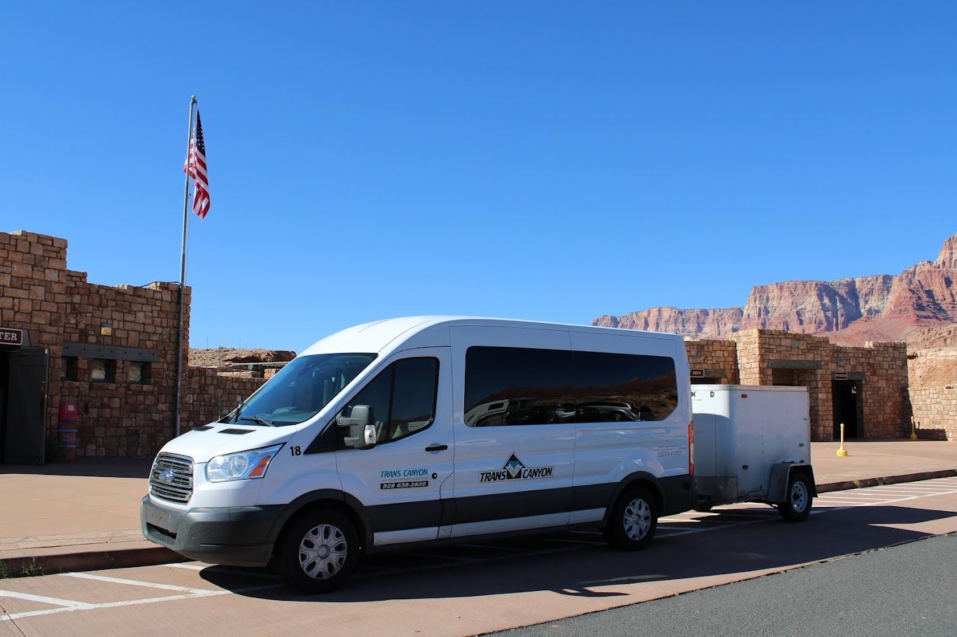 A white van with a trailer attached to it is parked in front of a stone building.