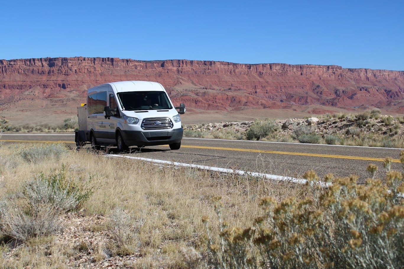 A white van is driving down a desert road.