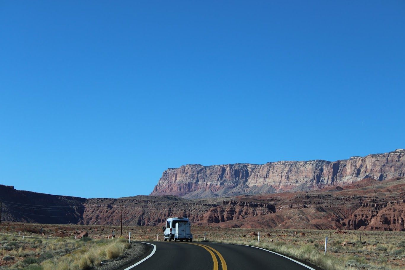A white van is driving down a desert road