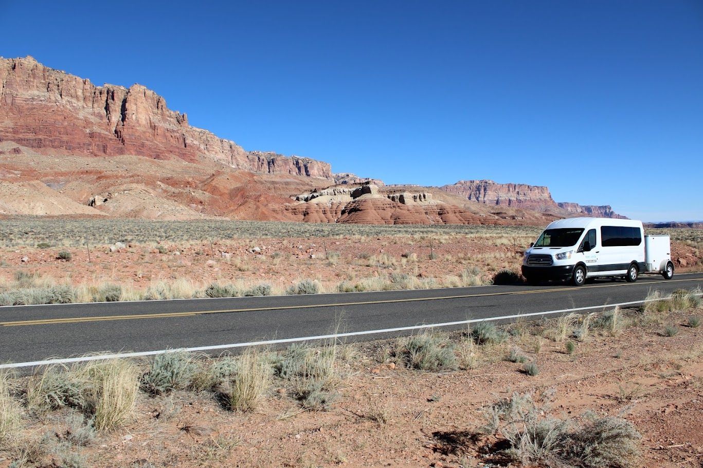 A white van is parked on the side of the road in the desert.