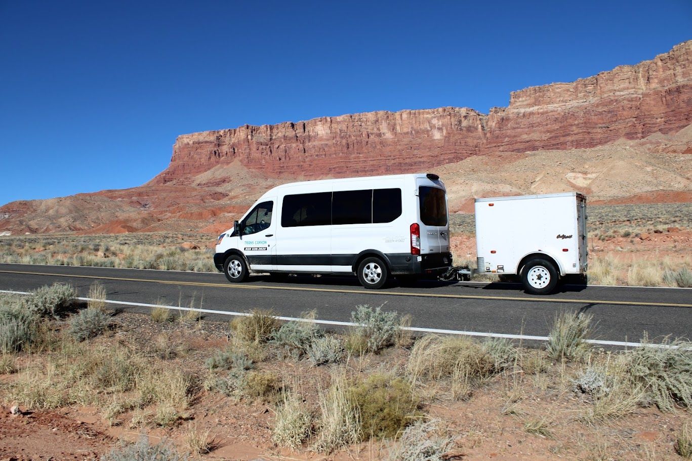 A white van is towing a trailer down a desert road.