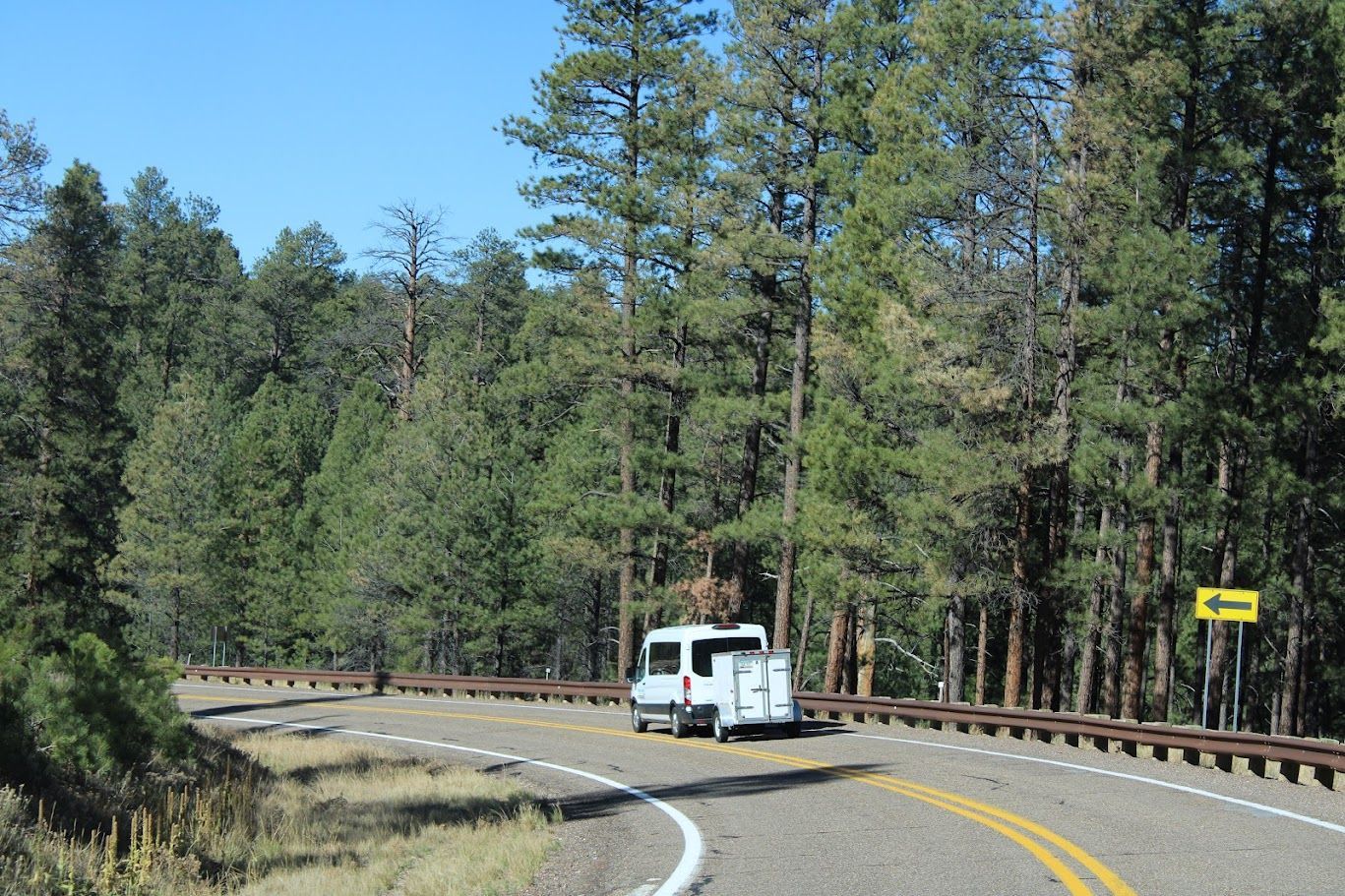 A white van is driving down a curvy road surrounded by trees.