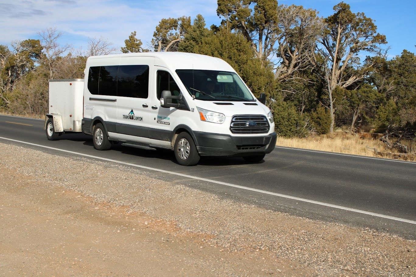 A white van is driving down a road with a trailer attached to it.