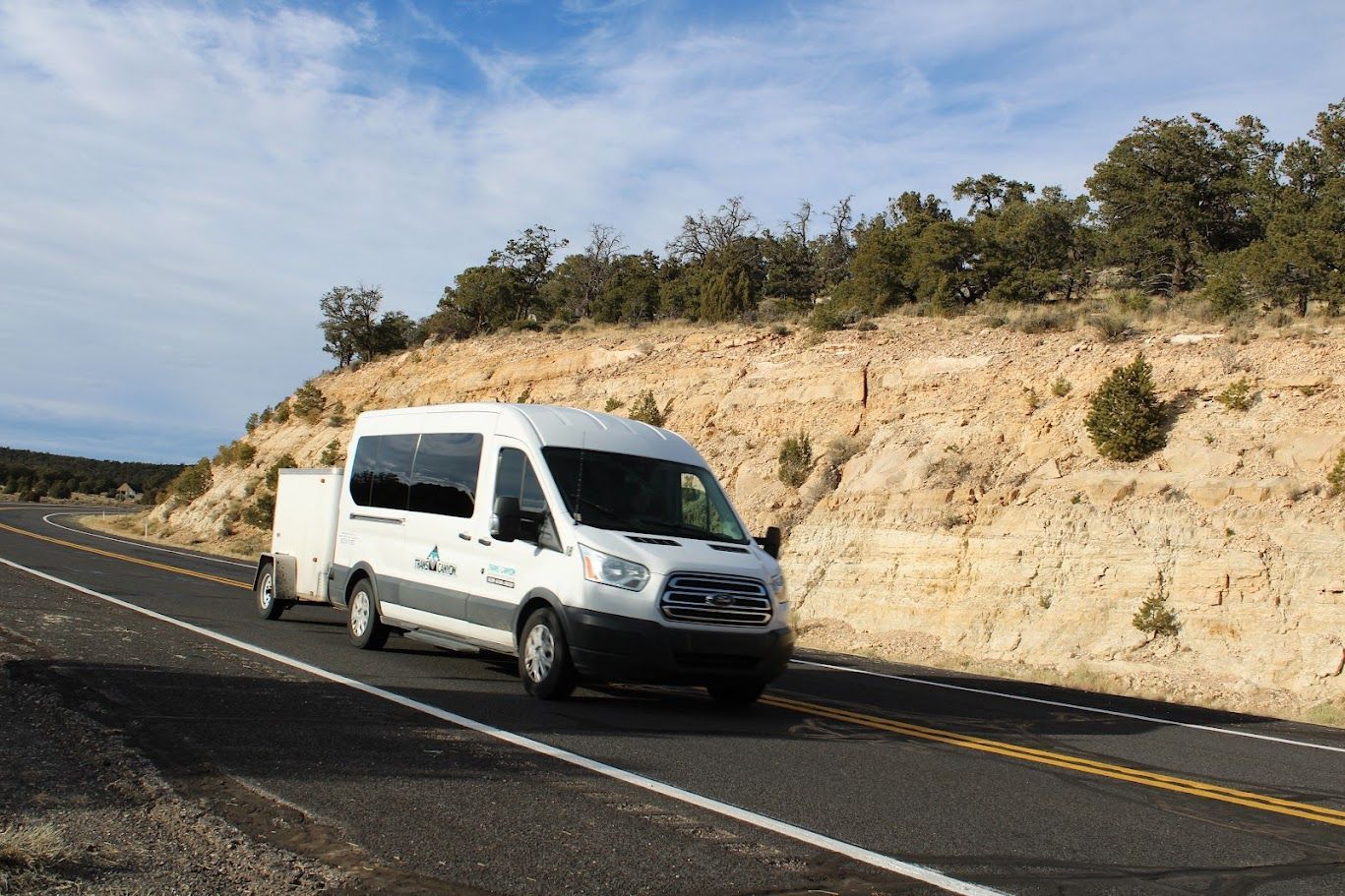 A white van is driving down a road with a trailer attached to it.