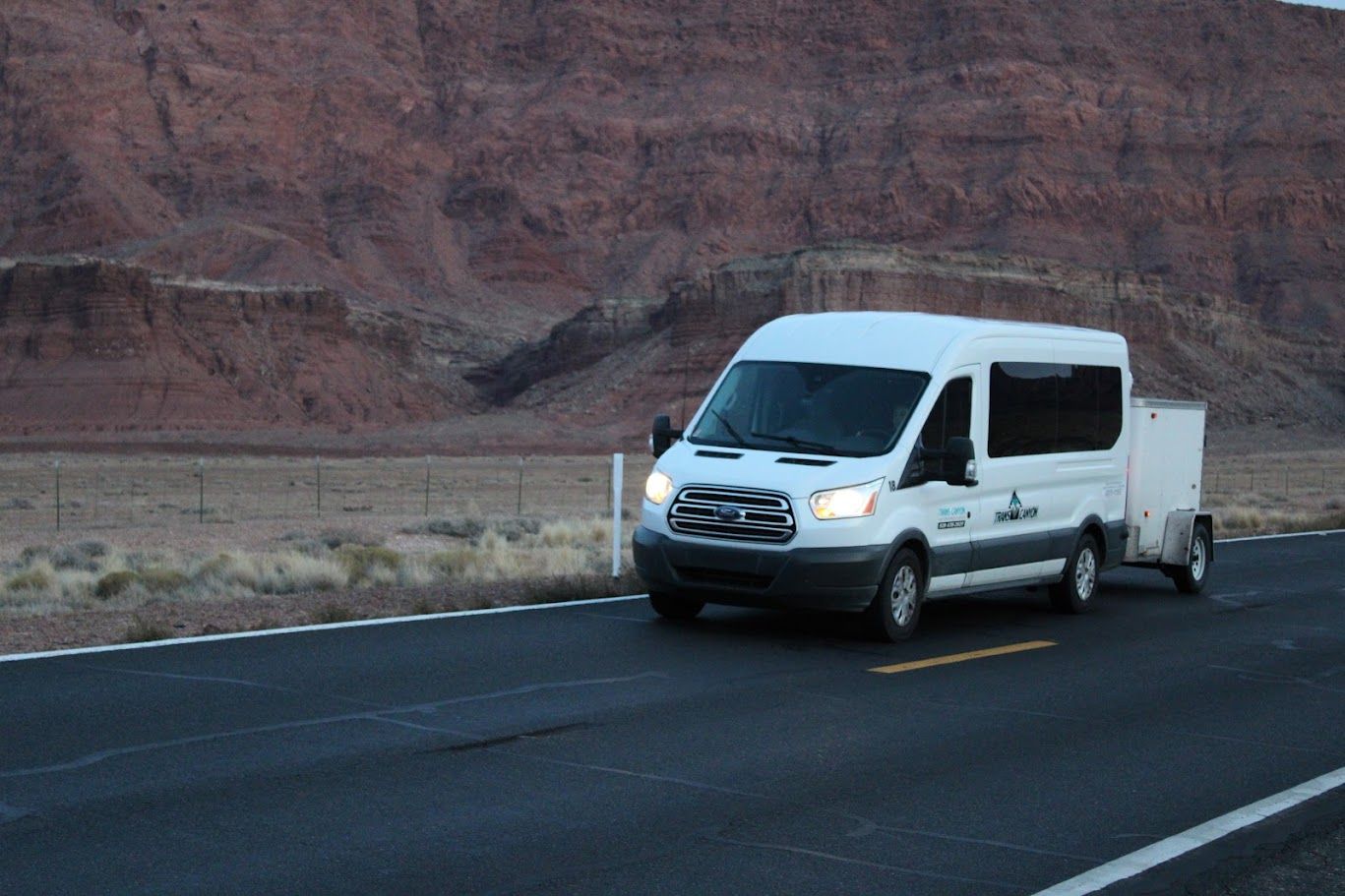 A white van is driving down a road with a trailer attached to it.