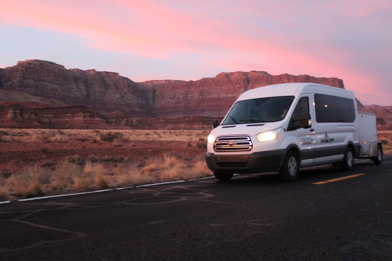 A white van is parked on the side of the road in the desert.