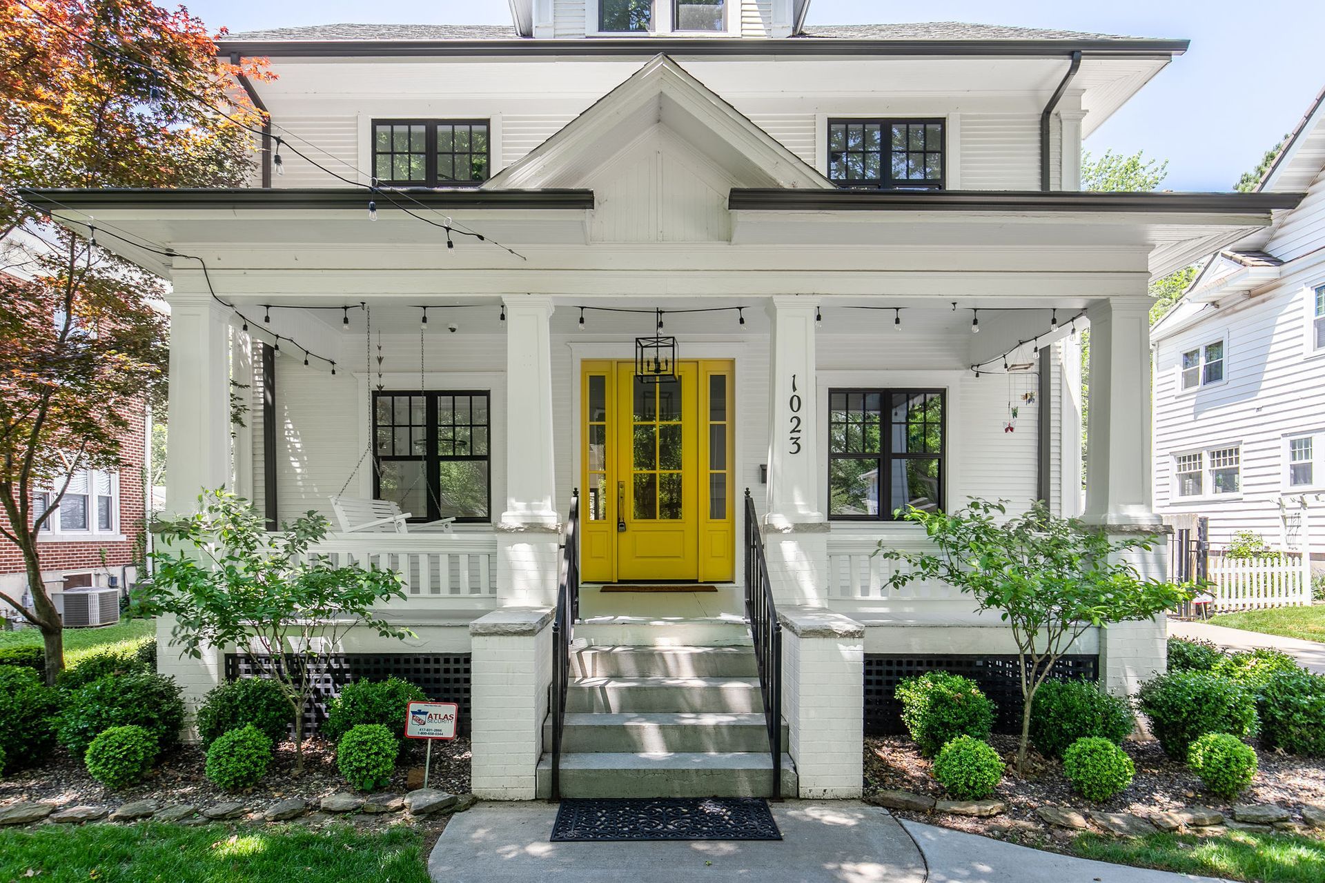 Brick house entrance with a bright red door, black railing, stone steps, and open white shutters