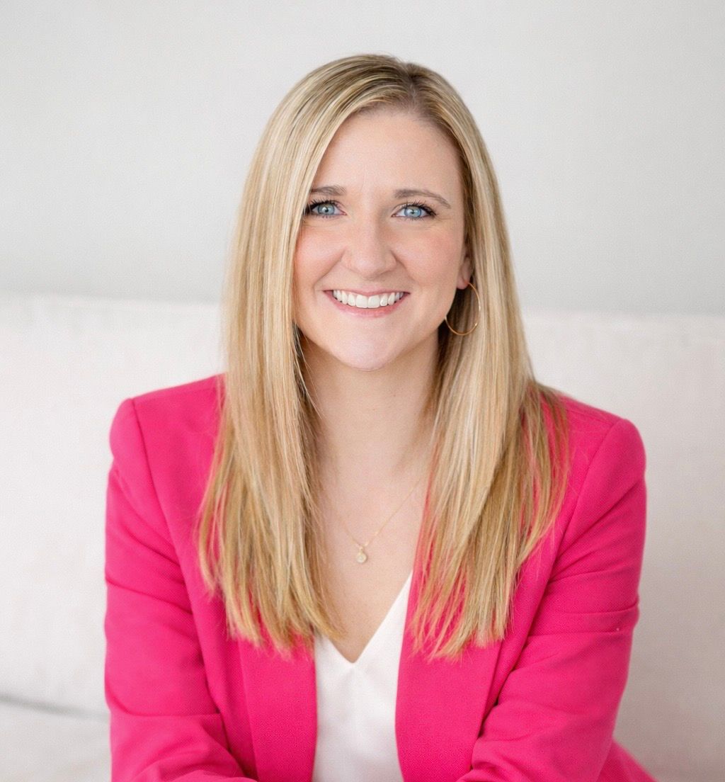 Smiling woman in a bright pink blazer against a light gray background