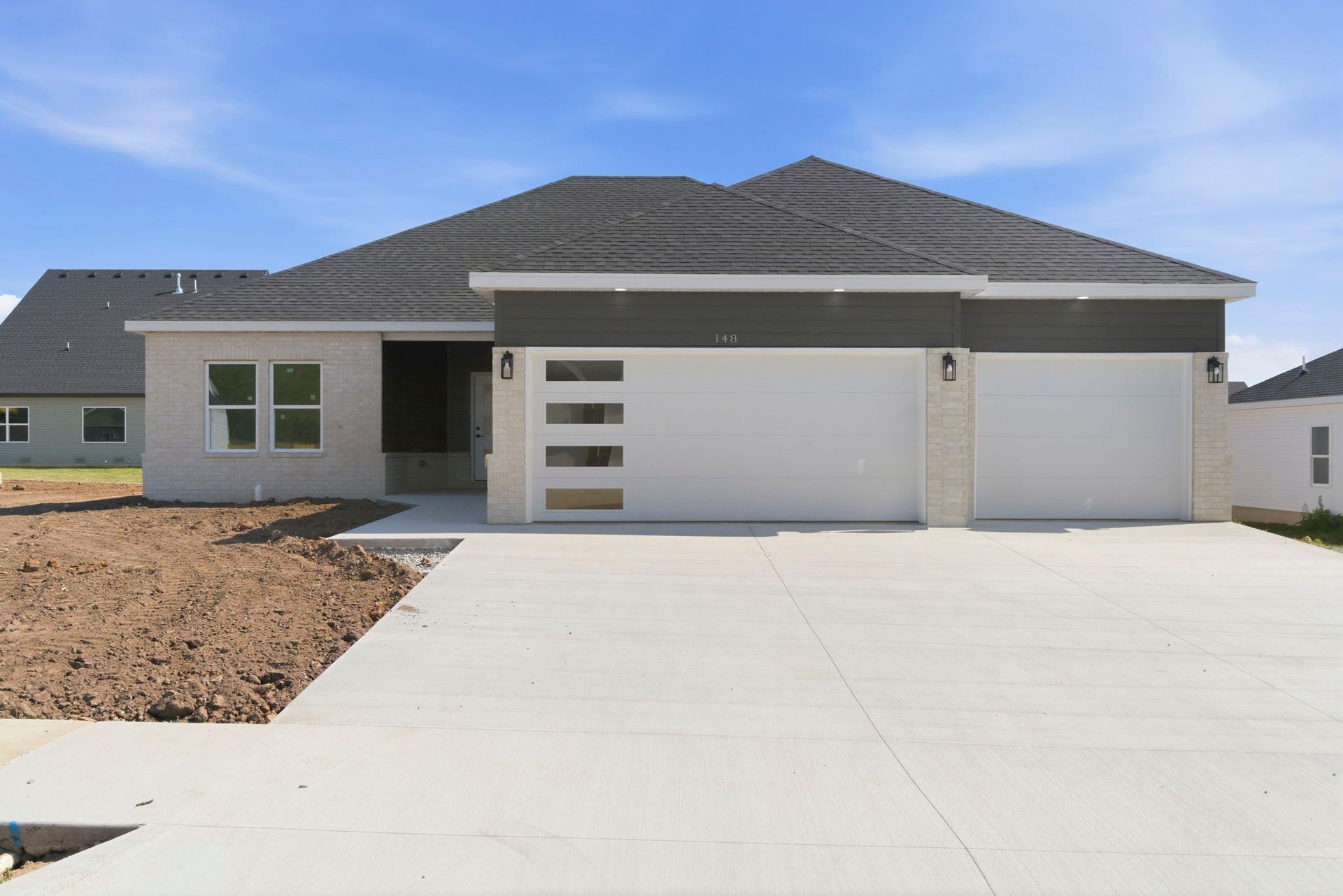Modern single-story house with gray roof, white garage, and wide concrete driveway