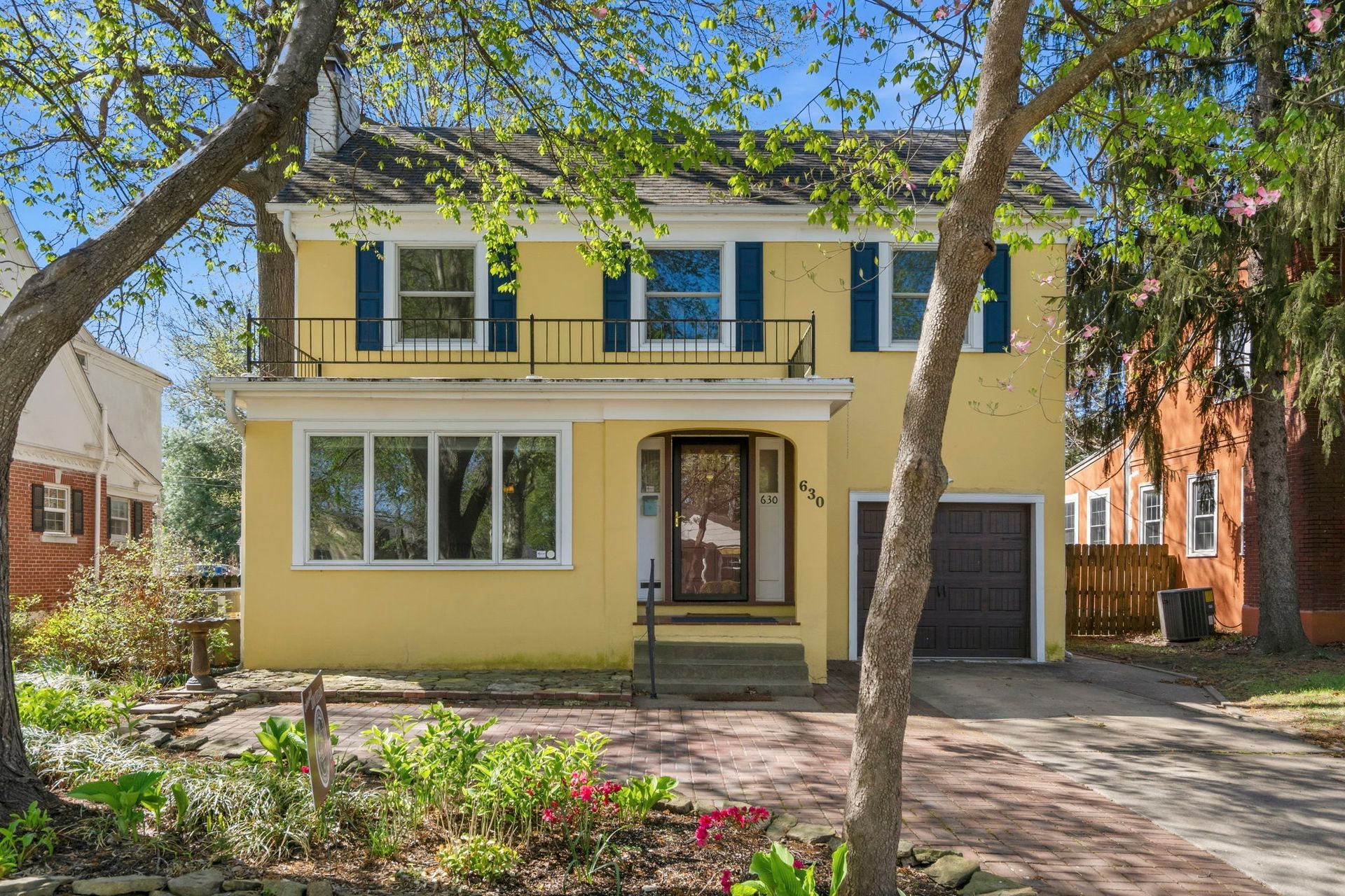 Yellow colonial style home with pink flower  and hosta landscaping and green trees with blue skies