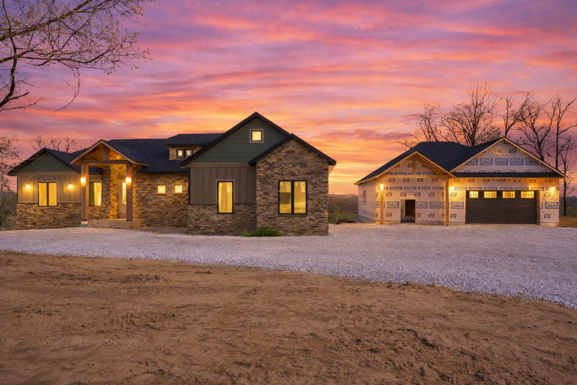 Stone house and detached garage lit at dusk beneath a pink-orange sunset sky.