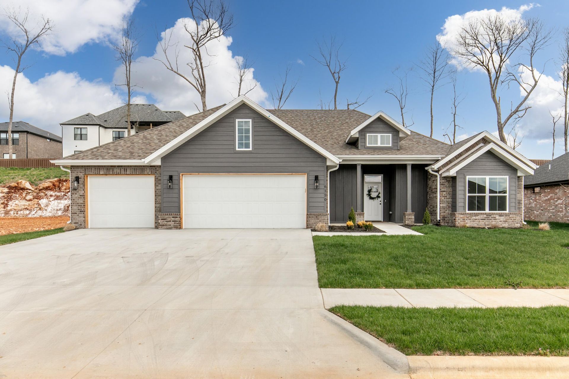 Single-story gray suburban house with three-car garage, front lawn, and wide concrete driveway.