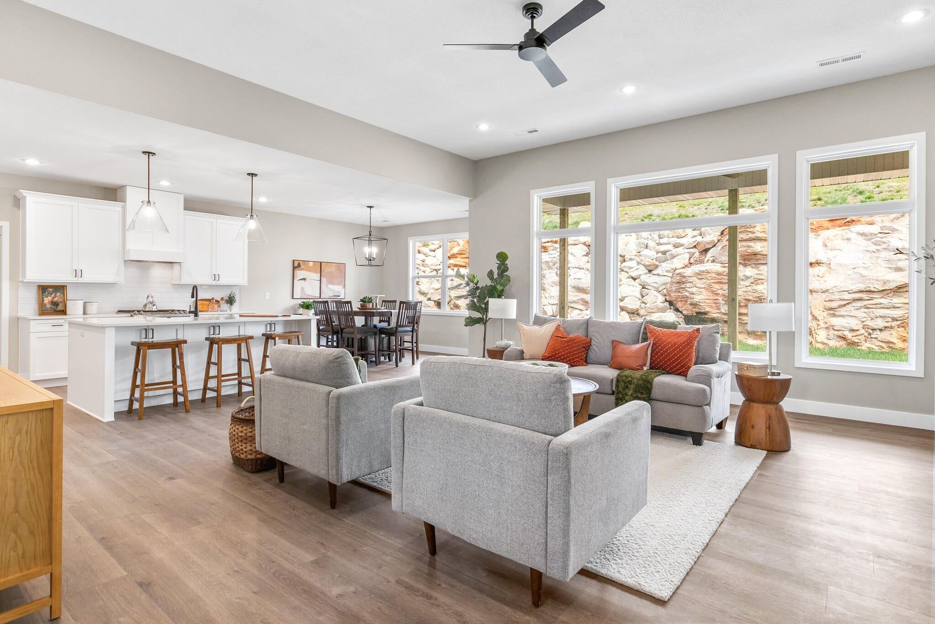 Bright open-concept living room with gray sofas, kitchen island stools, and large windows.