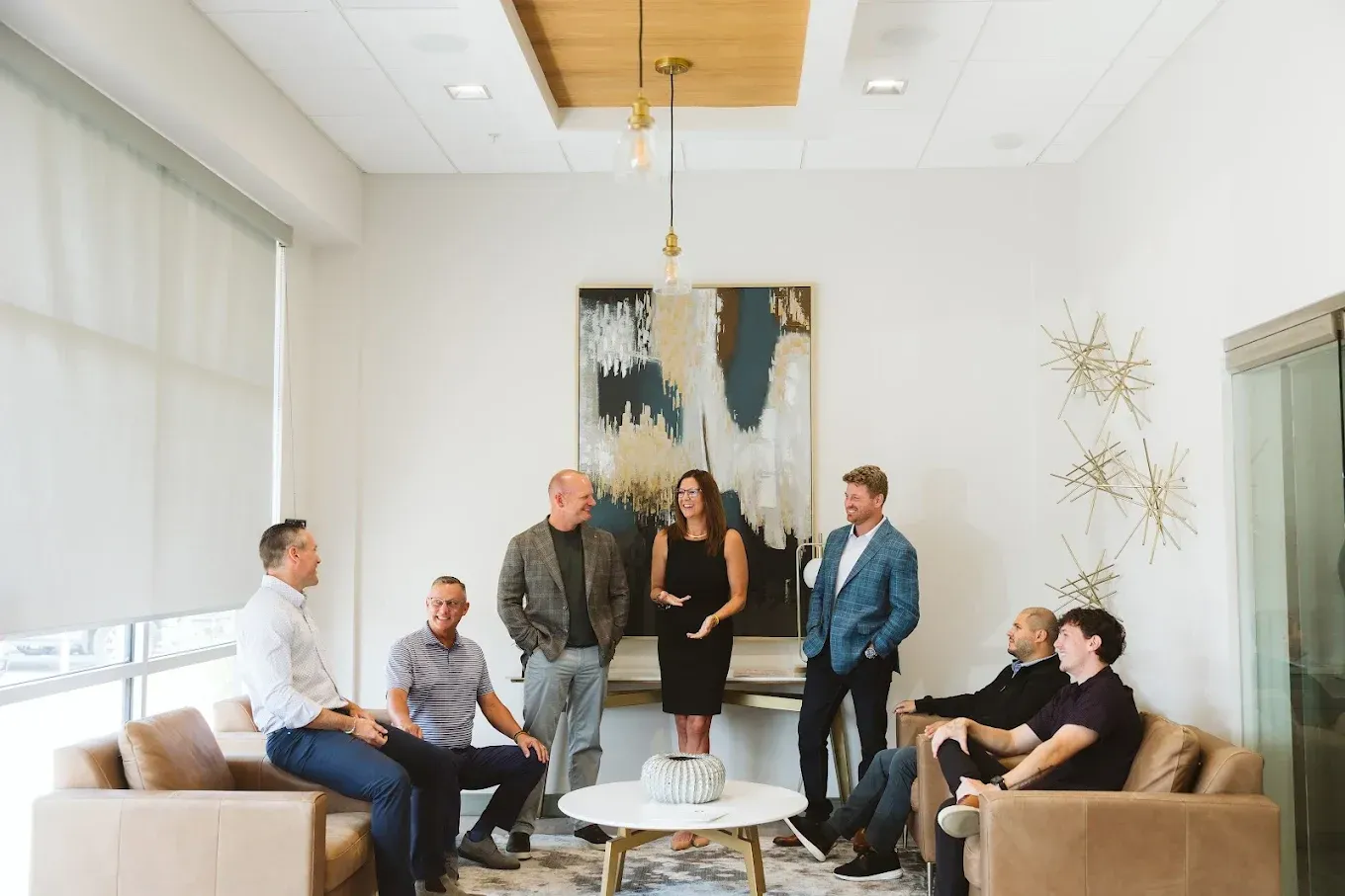 Group of people standing and sitting in a bright modern living room around a coffee table