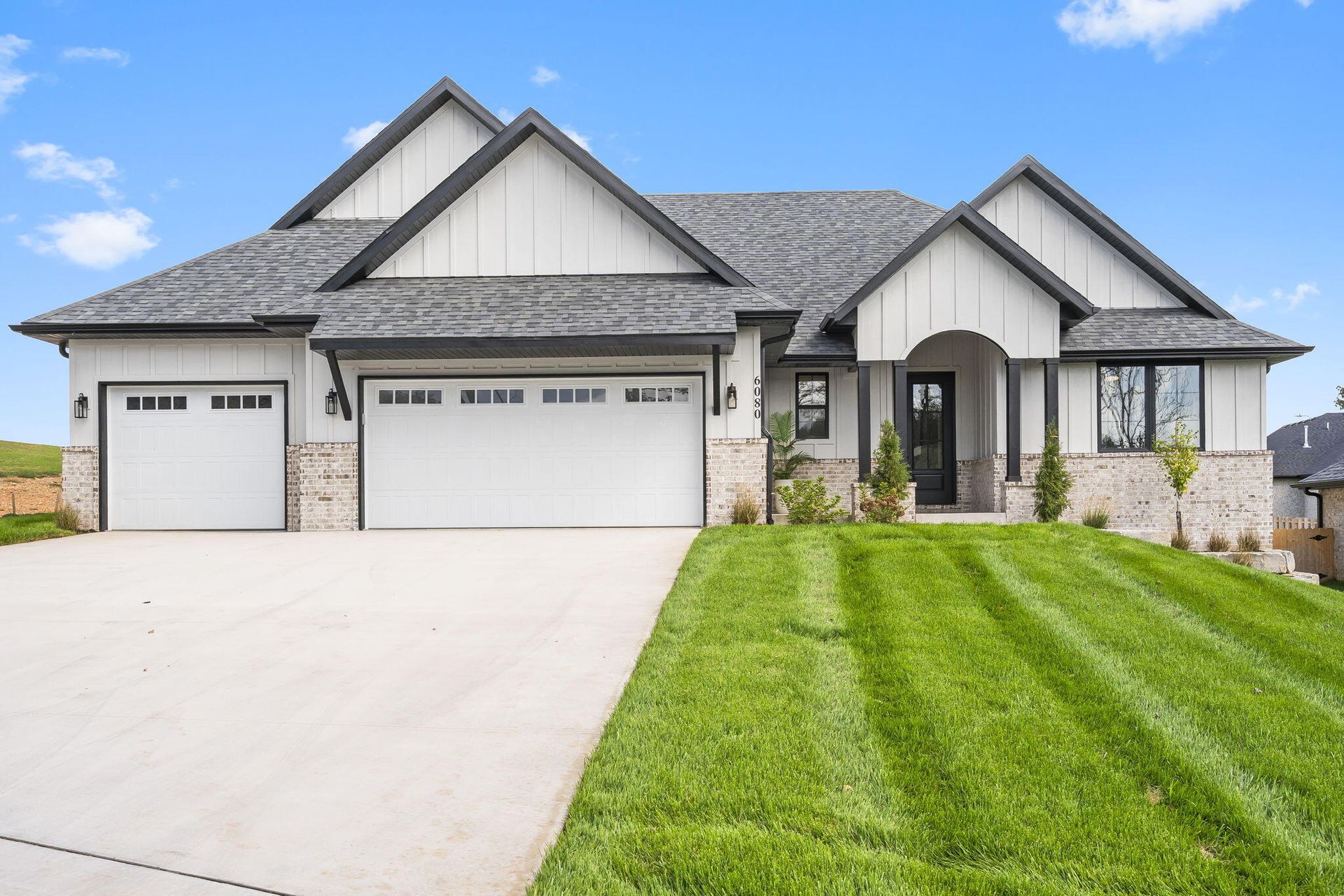 Modern gray suburban house with three-car garage, white driveway, and green lawn under a blue sky