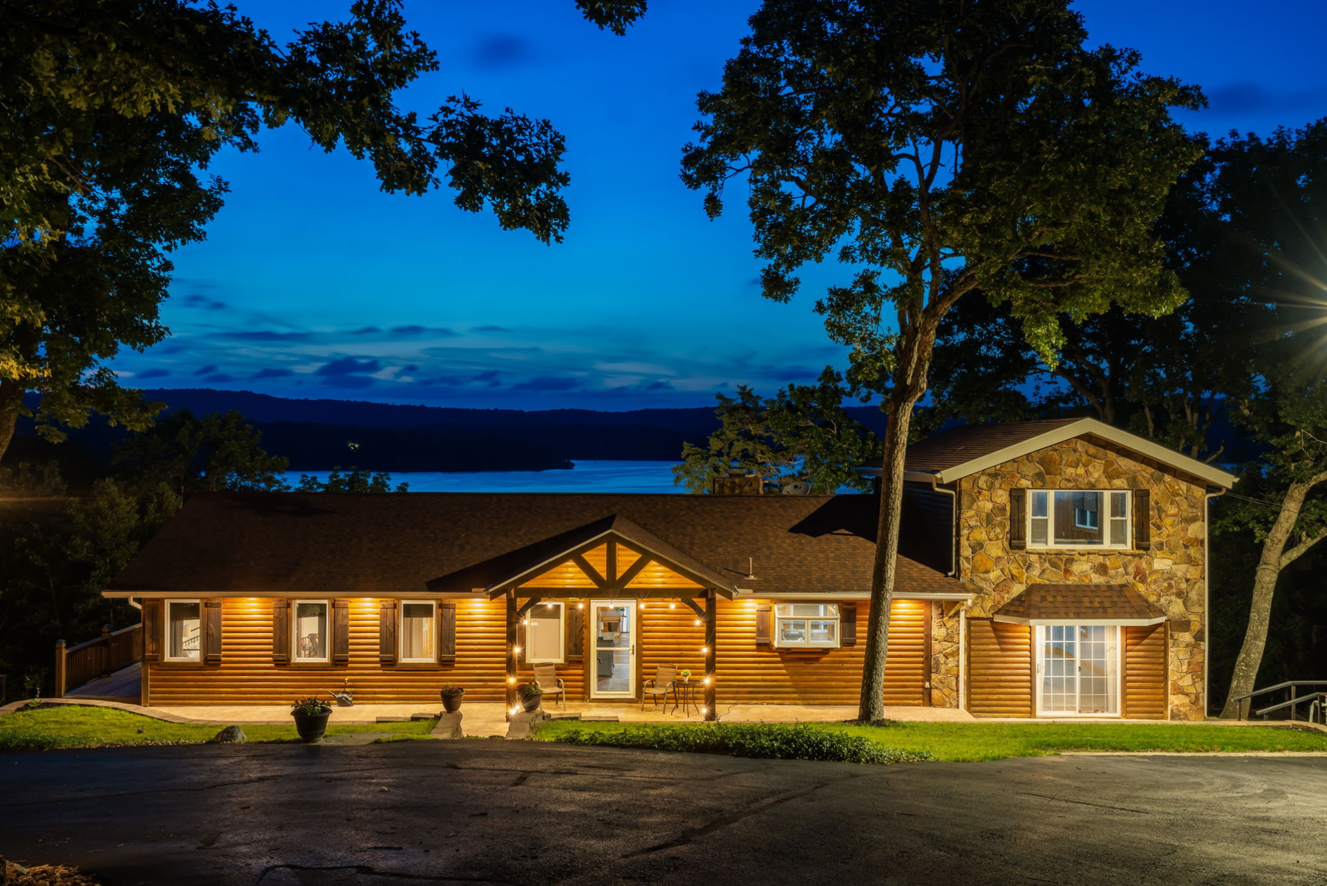 Lakefront cabin surrounded by trees at sunset, overlooking calm water and distant hills