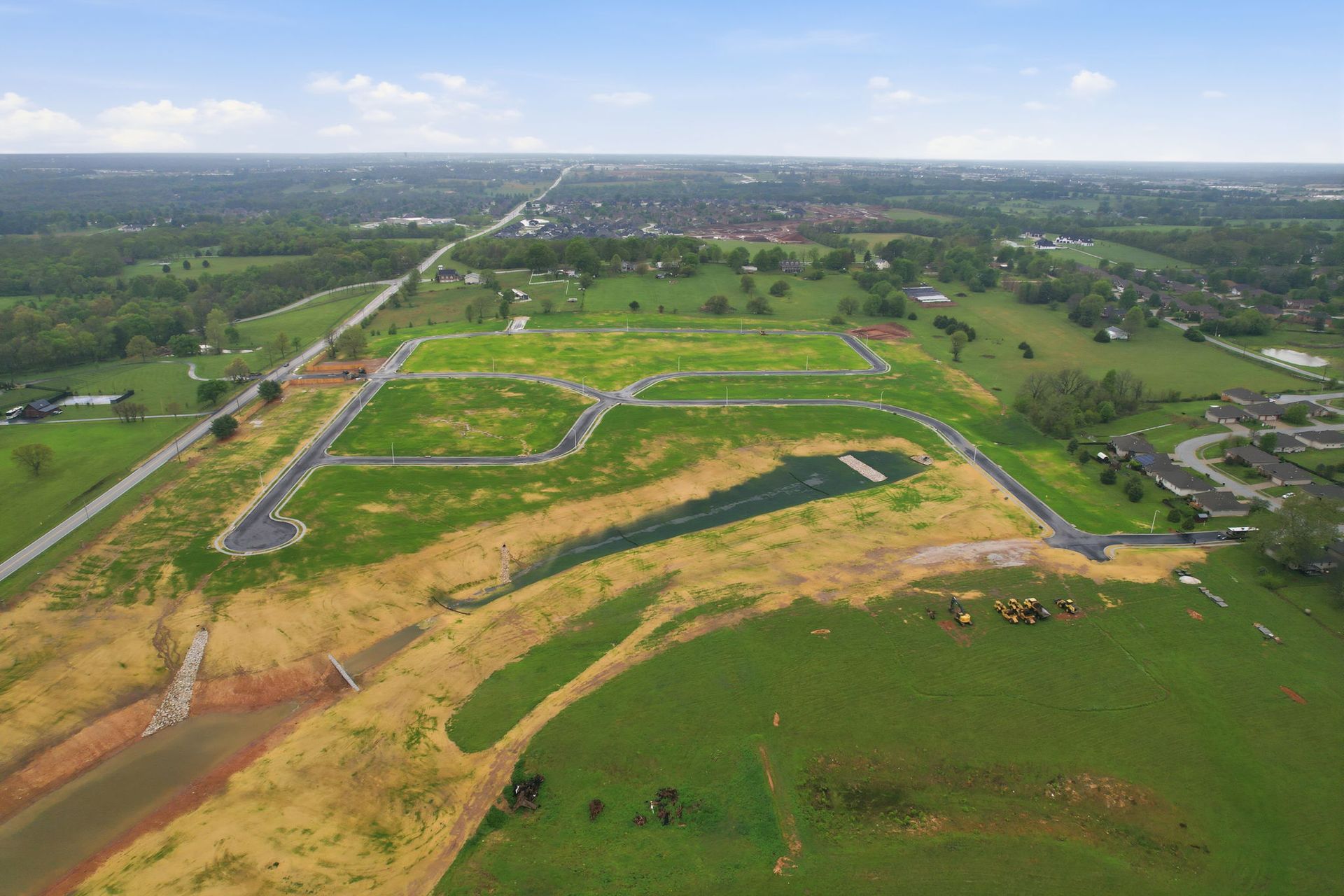 Aerial view of a green countryside field with scattered trees under a blue sky