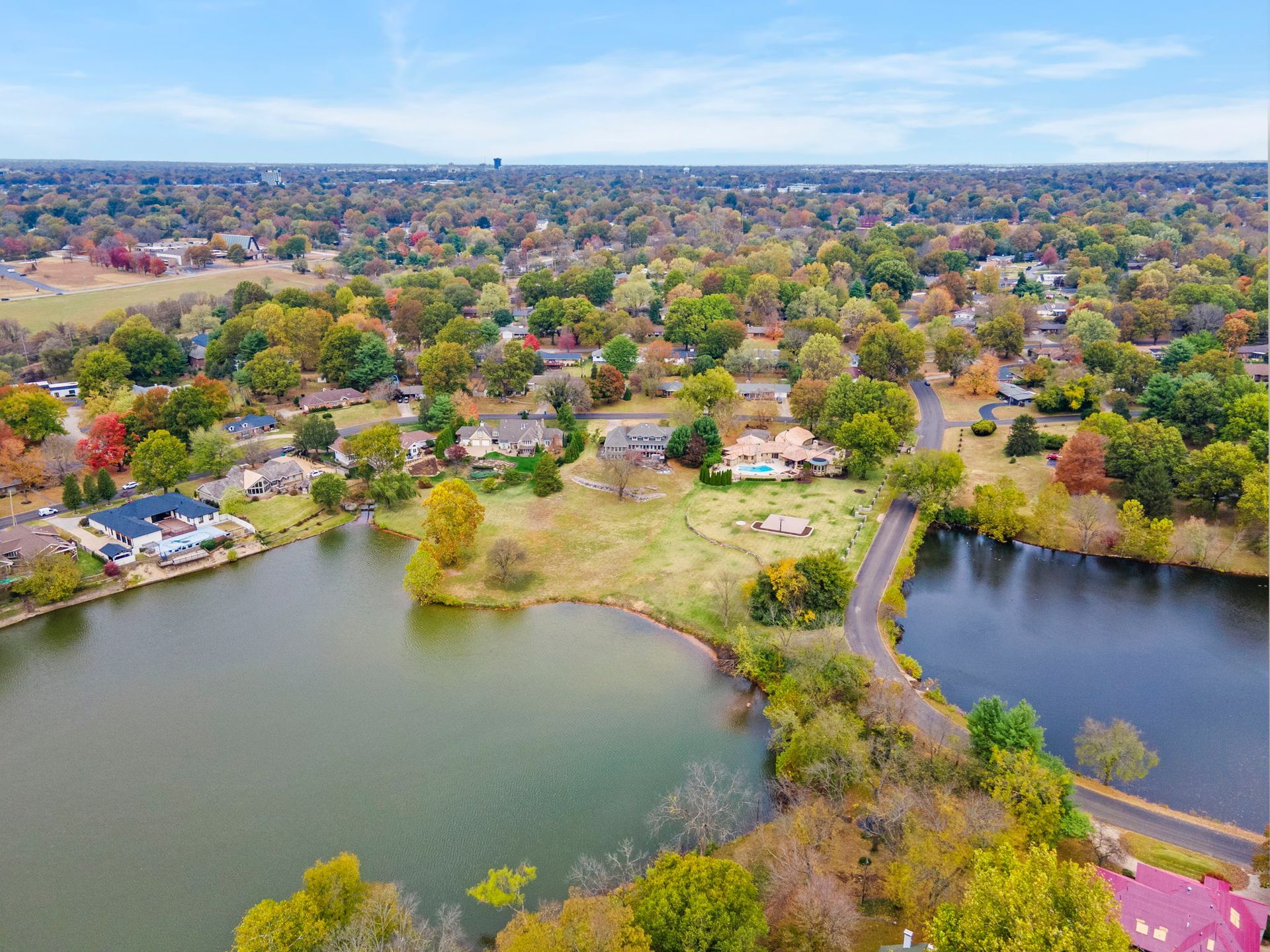 Aerial view of a lakeside neighborhood with trees, houses, and winding roads in autumn colors
