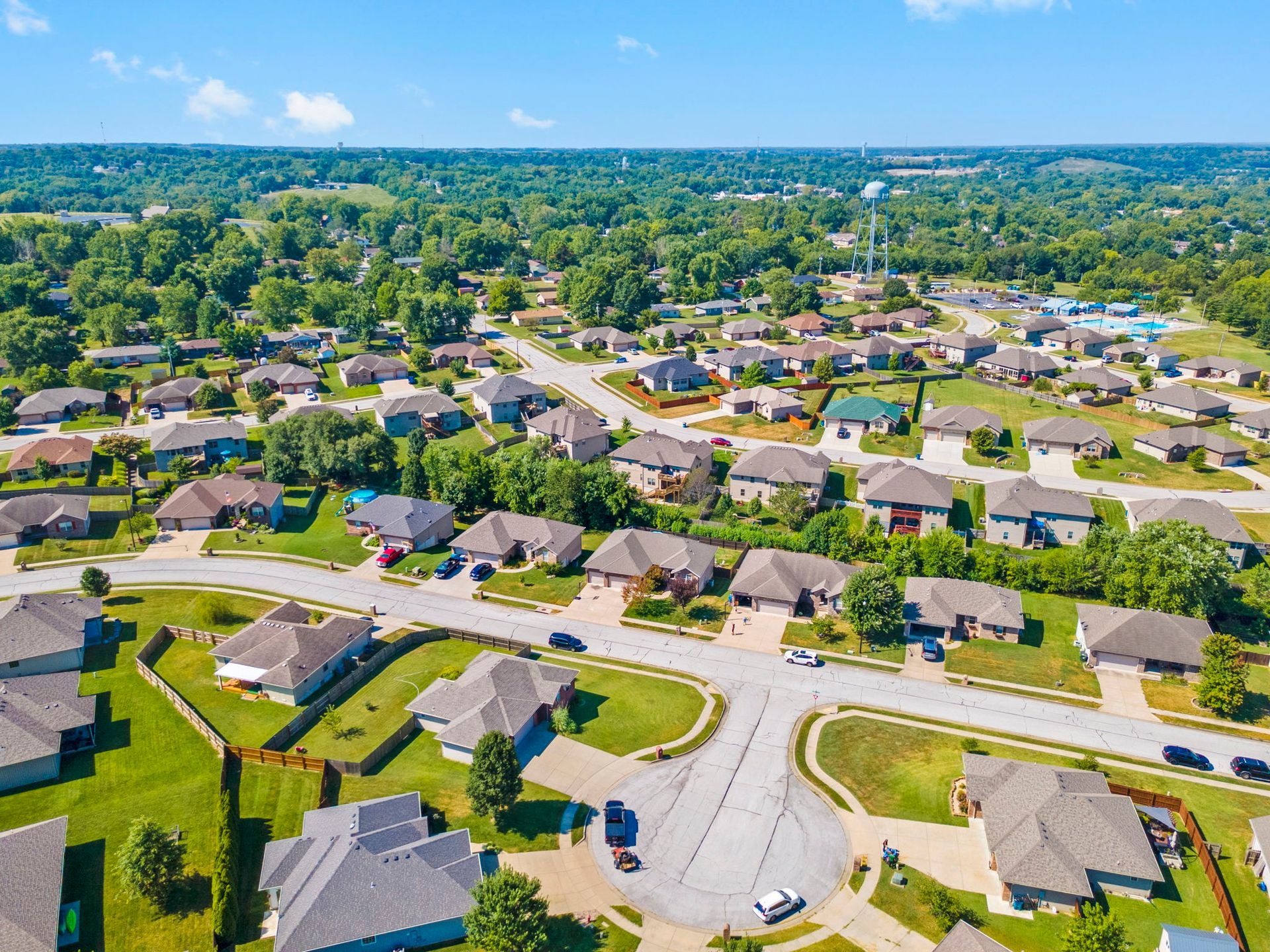 Aerial view of a suburban neighborhood with curved streets, houses, and trees under a clear blue sky