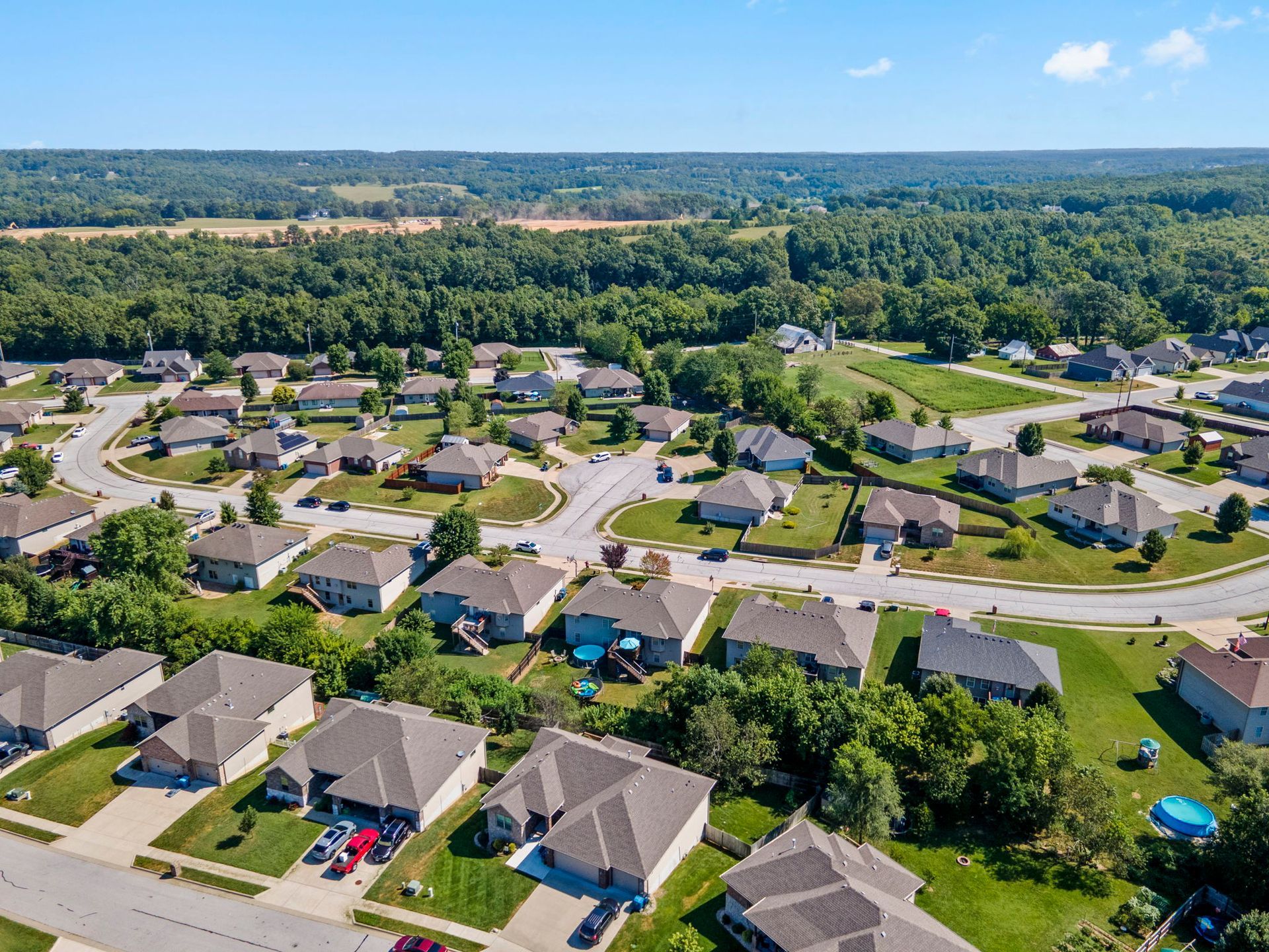 Aerial view of a suburban neighborhood with rows of houses, streets, and trees under a blue sky