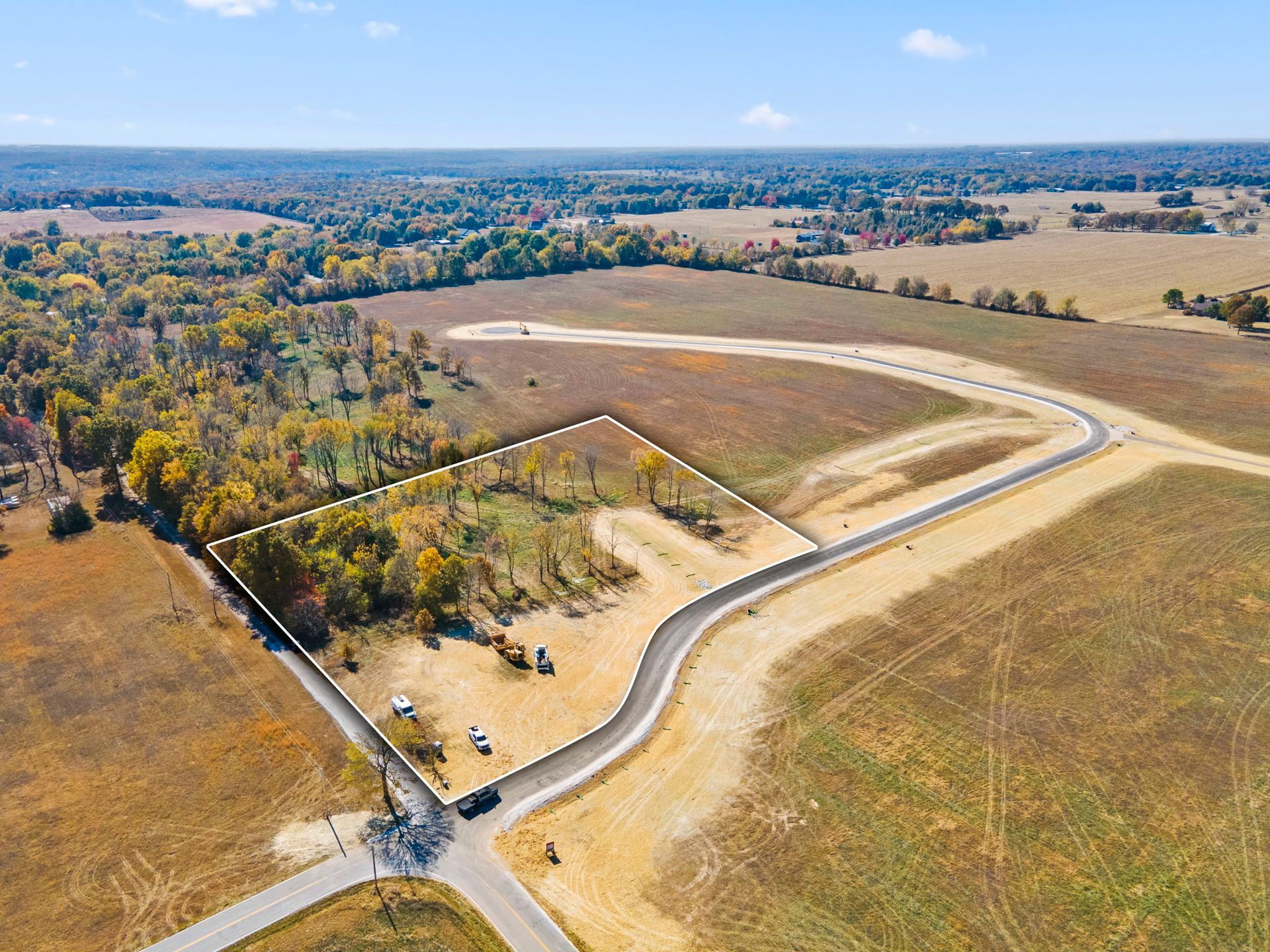 Aerial view of rural fields with a winding road and a fenced lot under a clear sky.