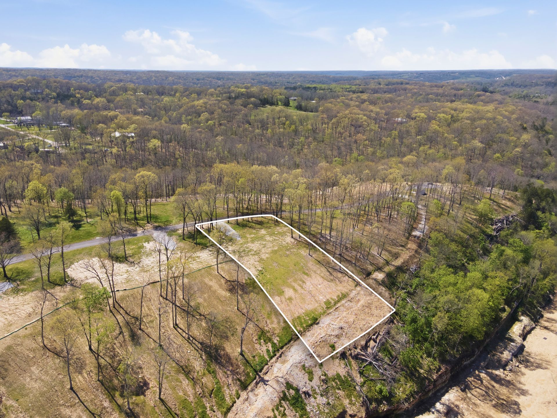 Aerial view of a wooded landscape with a fenced clearing and winding road.