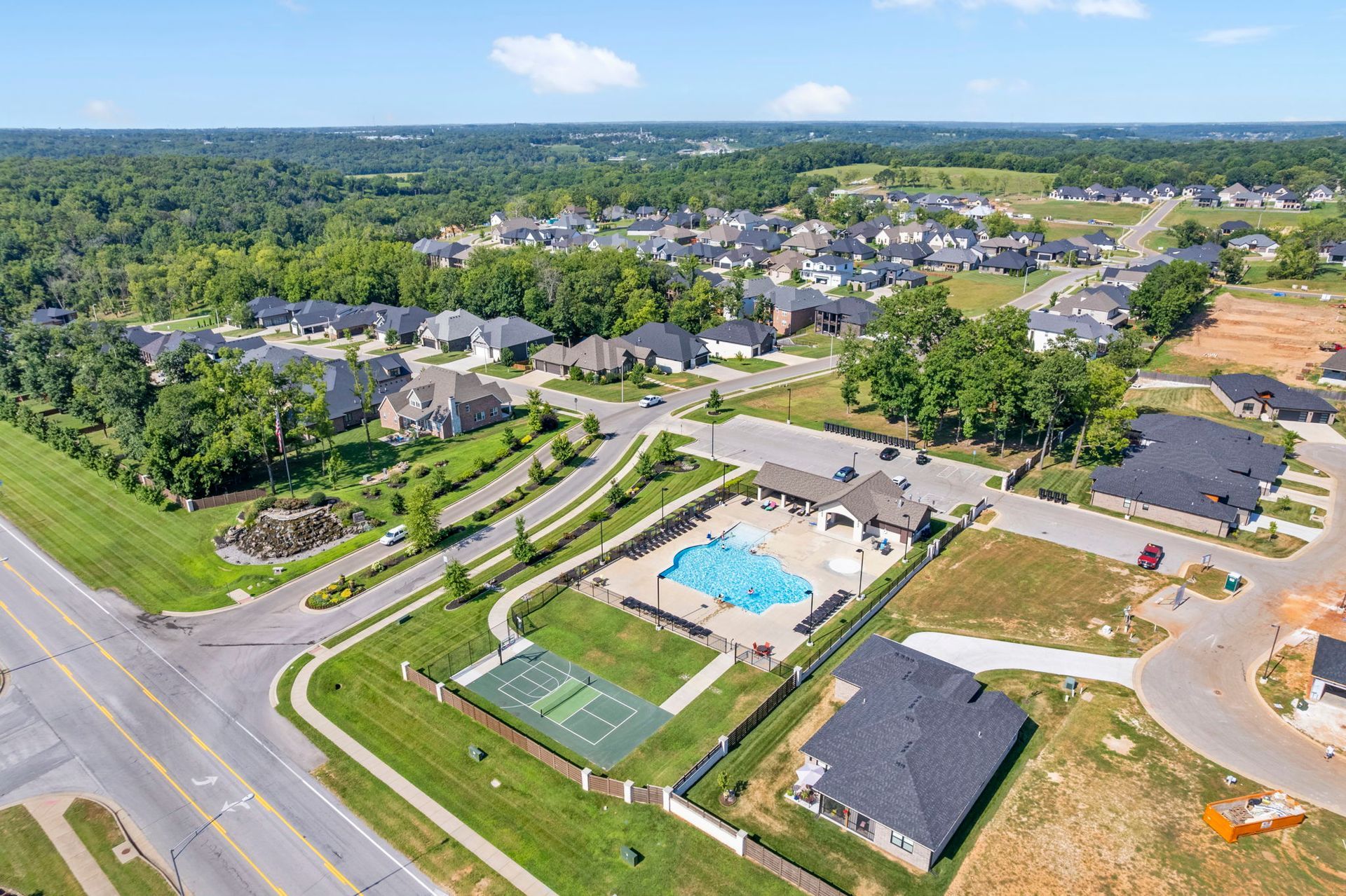 Aerial view of a suburban sports complex with tennis courts, a pool, parking lots, and surrounding homes.