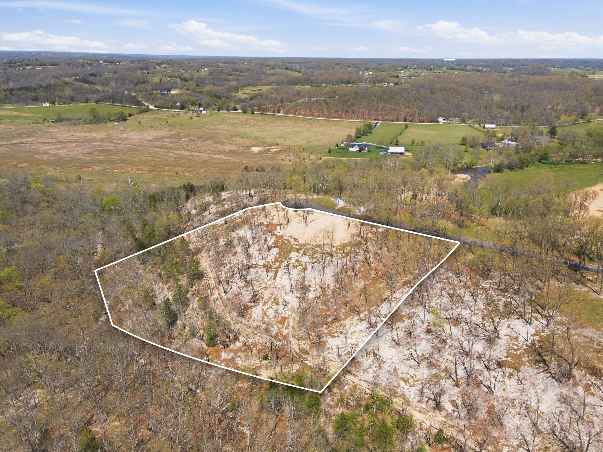 Outlined rocky hillside overlooking a wide grassy valley and distant trees under a cloudy sky
