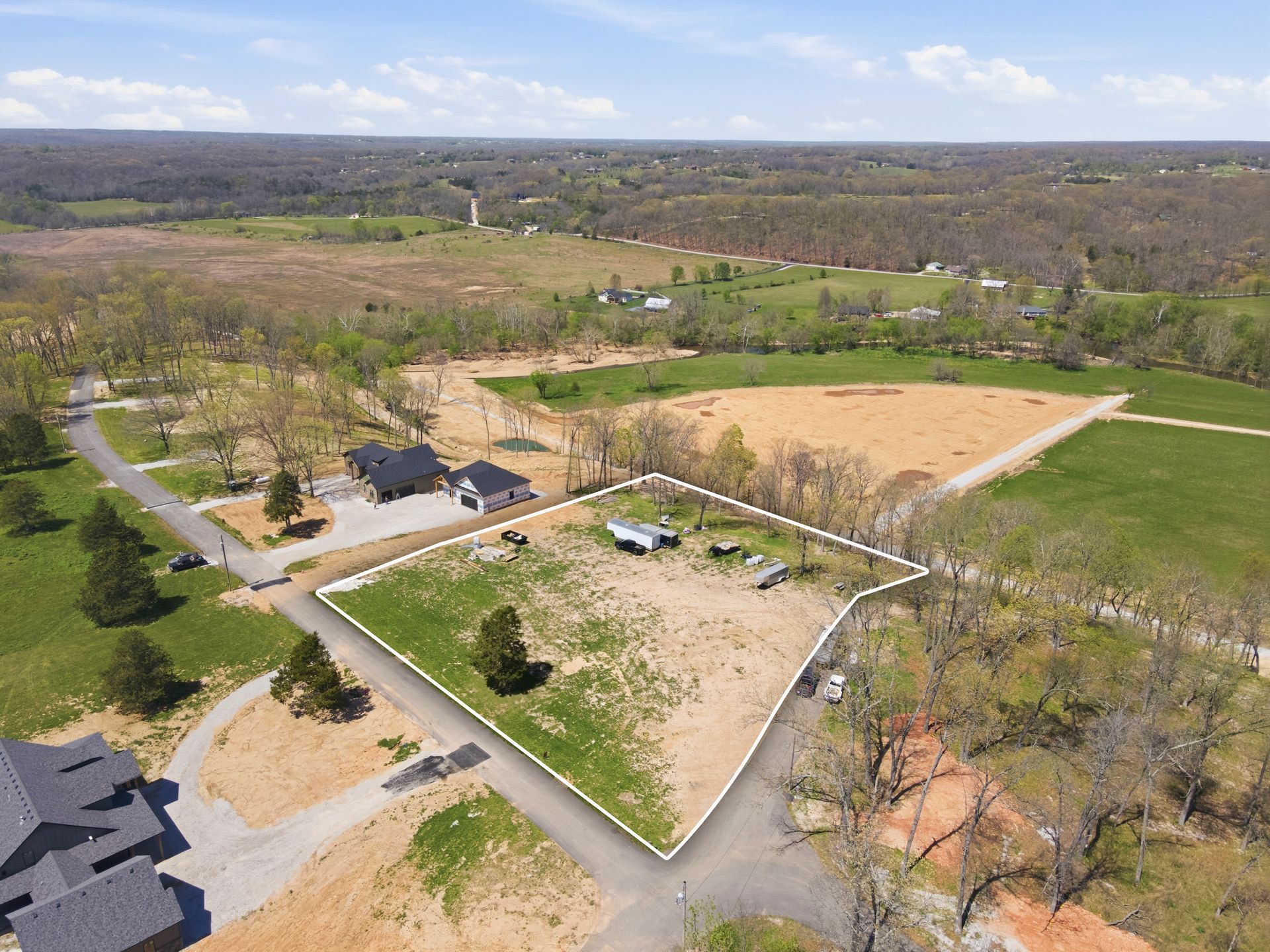 Aerial view of a rural property with fenced fields, trees, and a long driveway under a clear sky