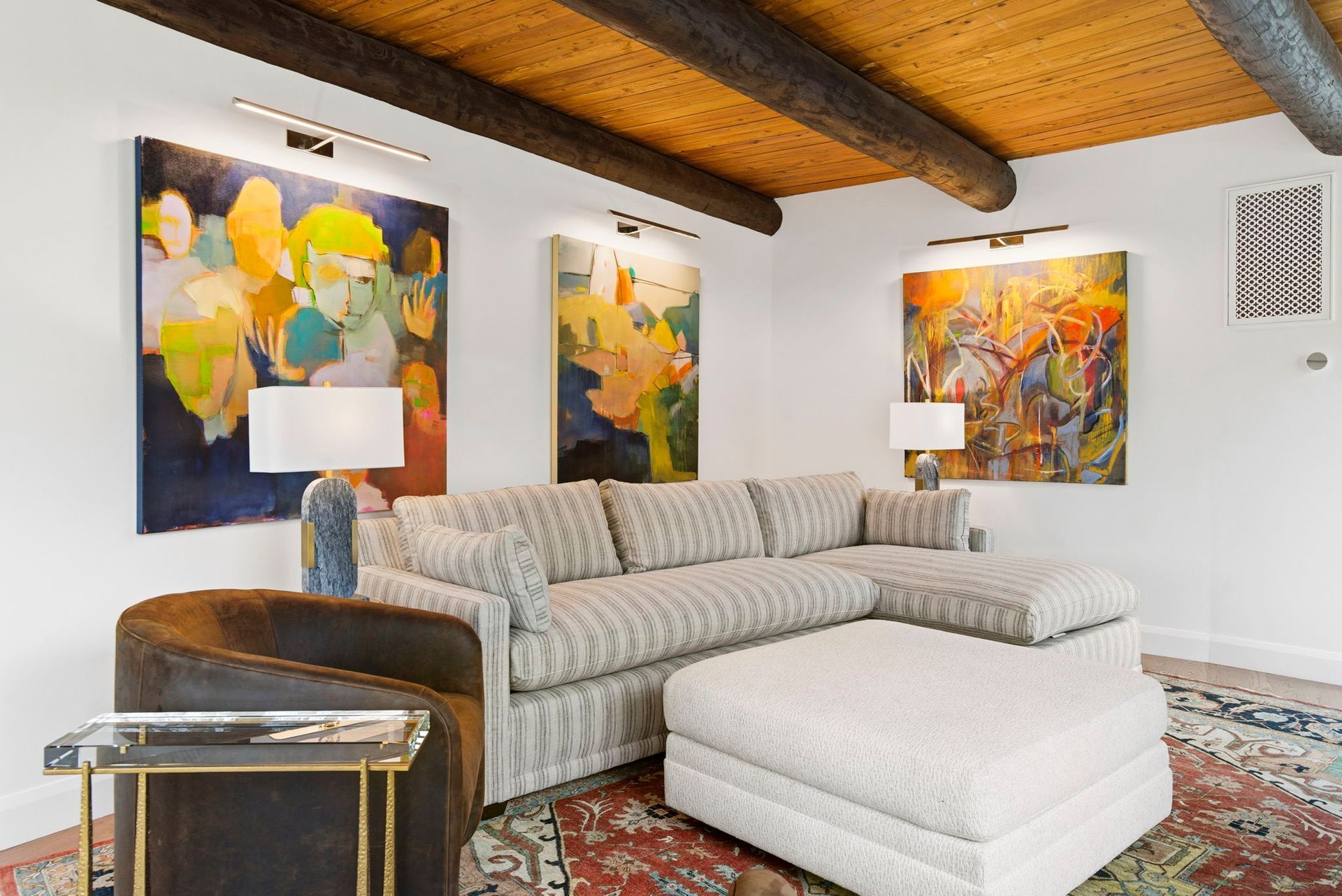Modern living room with beige sectional, colorful abstract art, wood ceiling, and patterned rug