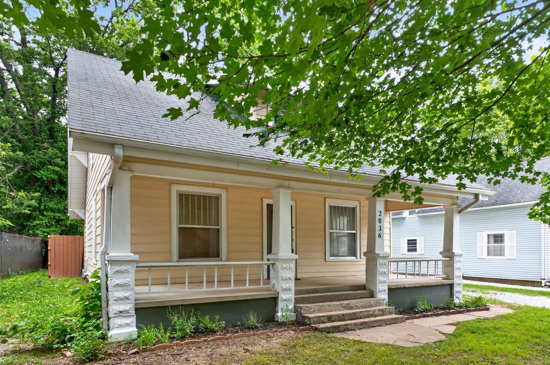 Older beige home with covered front porch and mature trees in Republic, Missouri.