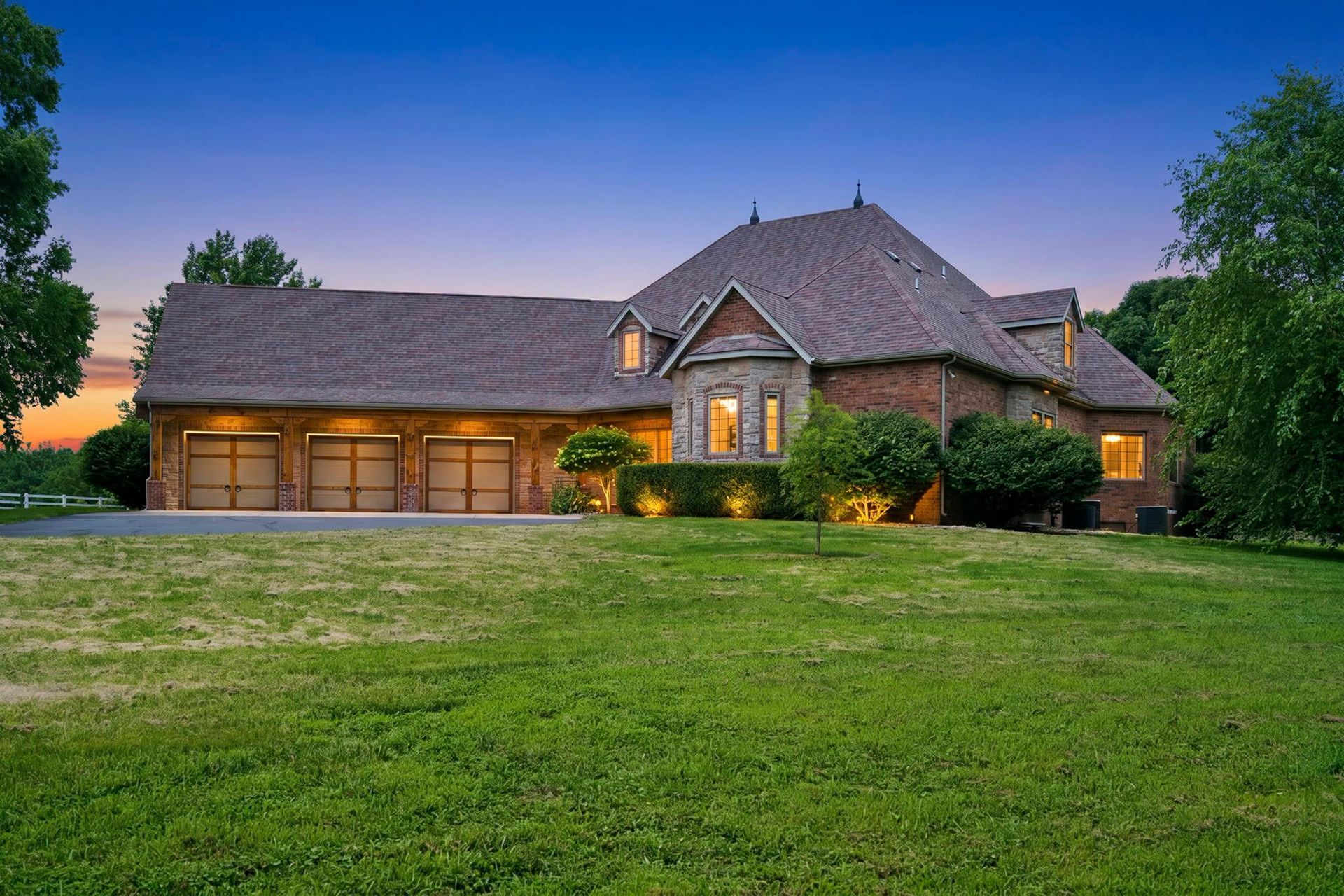 Large stone house with lit windows, three-car garage in Springfield, MO