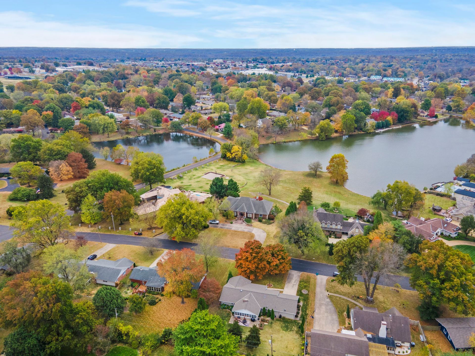 Aerial view of a suburban neighborhood with colorful autumn trees and a large pond nearby