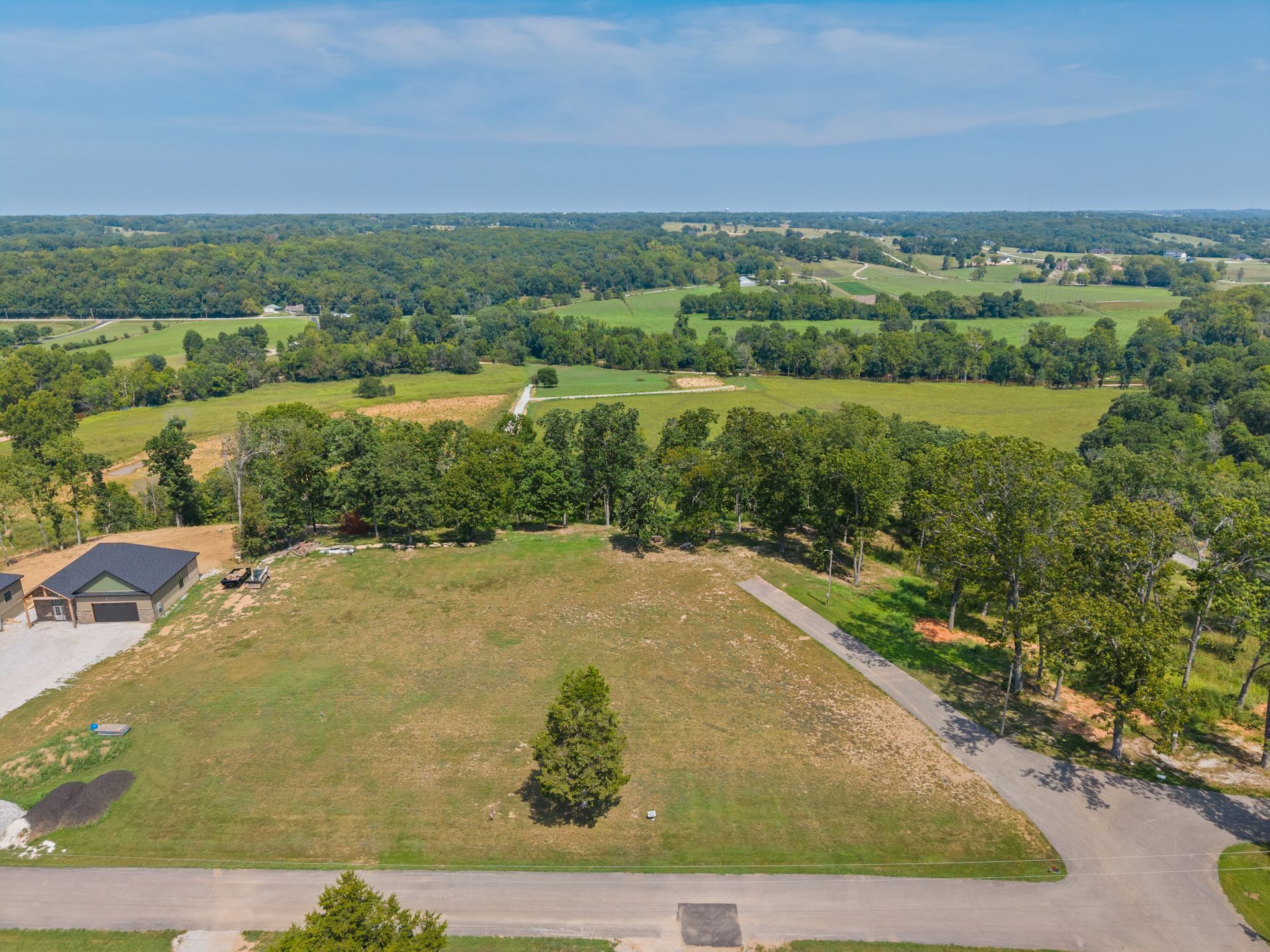 Aerial view of a rural property with fenced fields, trees, and a long driveway under a clear sky