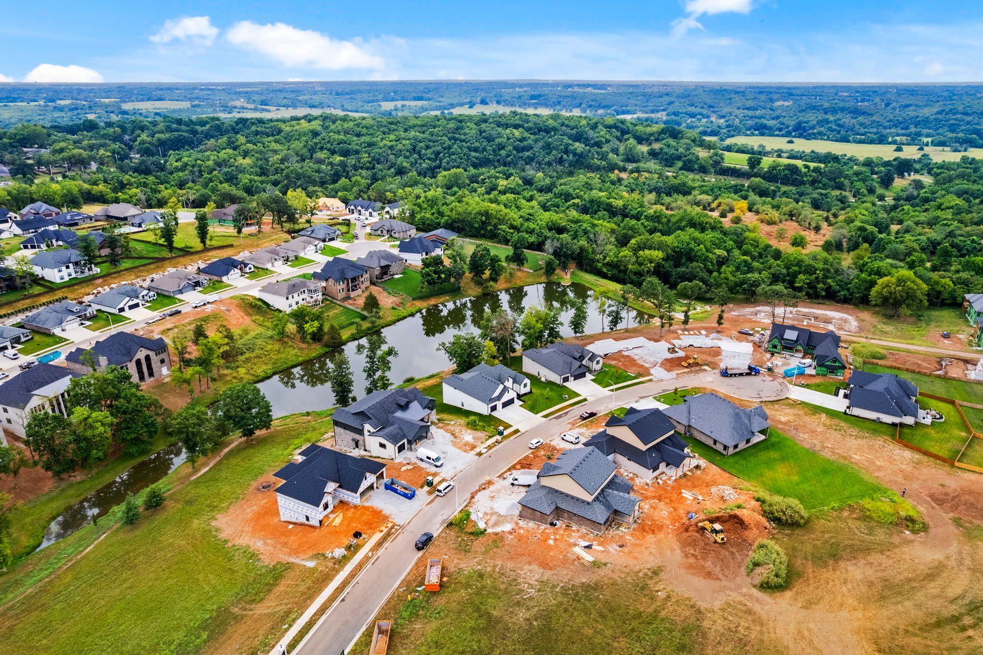 Aerial view of a suburban neighborhood with houses, roads, and dense green trees beyond.