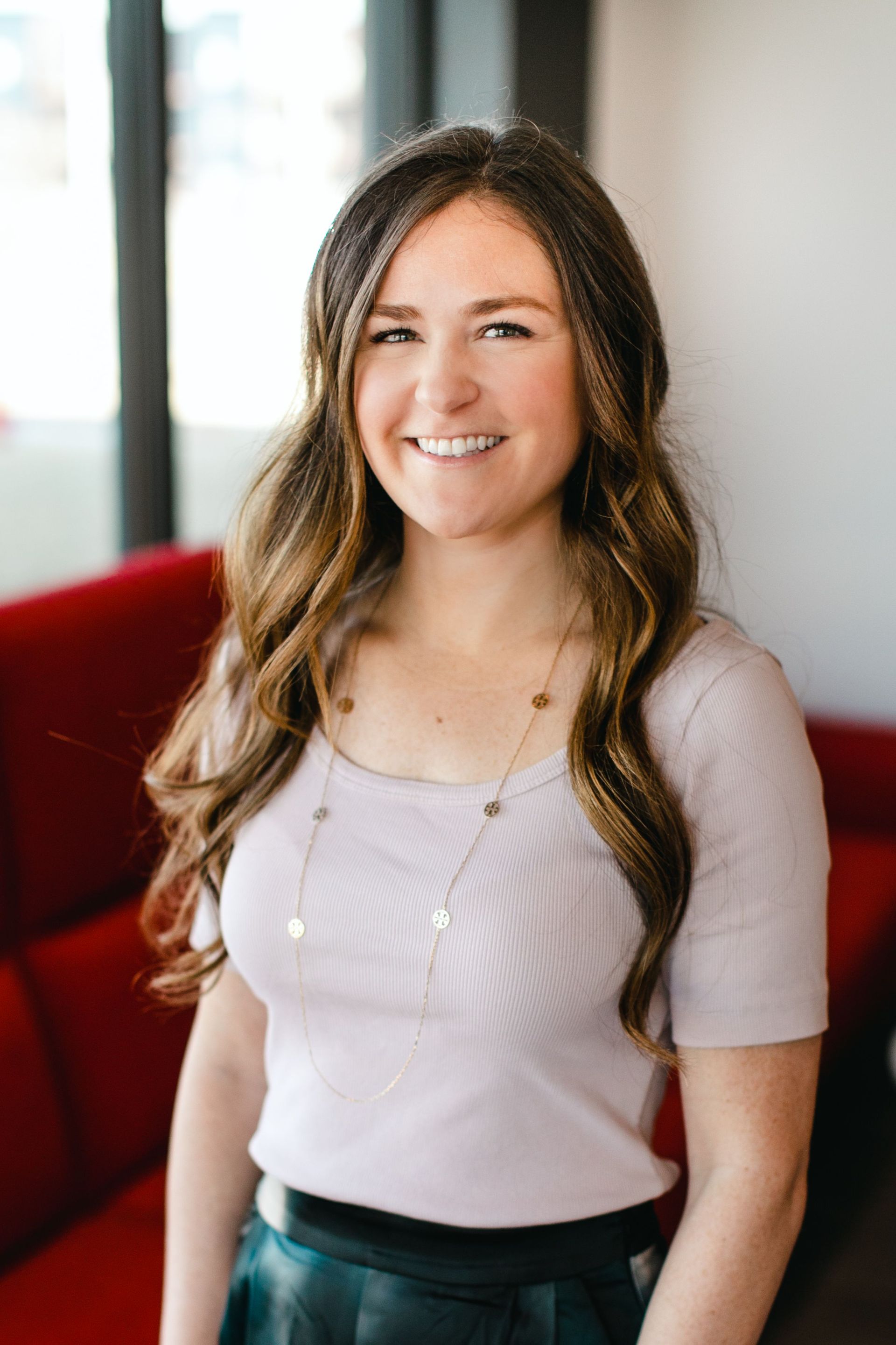 Smiling woman in a light lavender top standing indoors with a blurred background