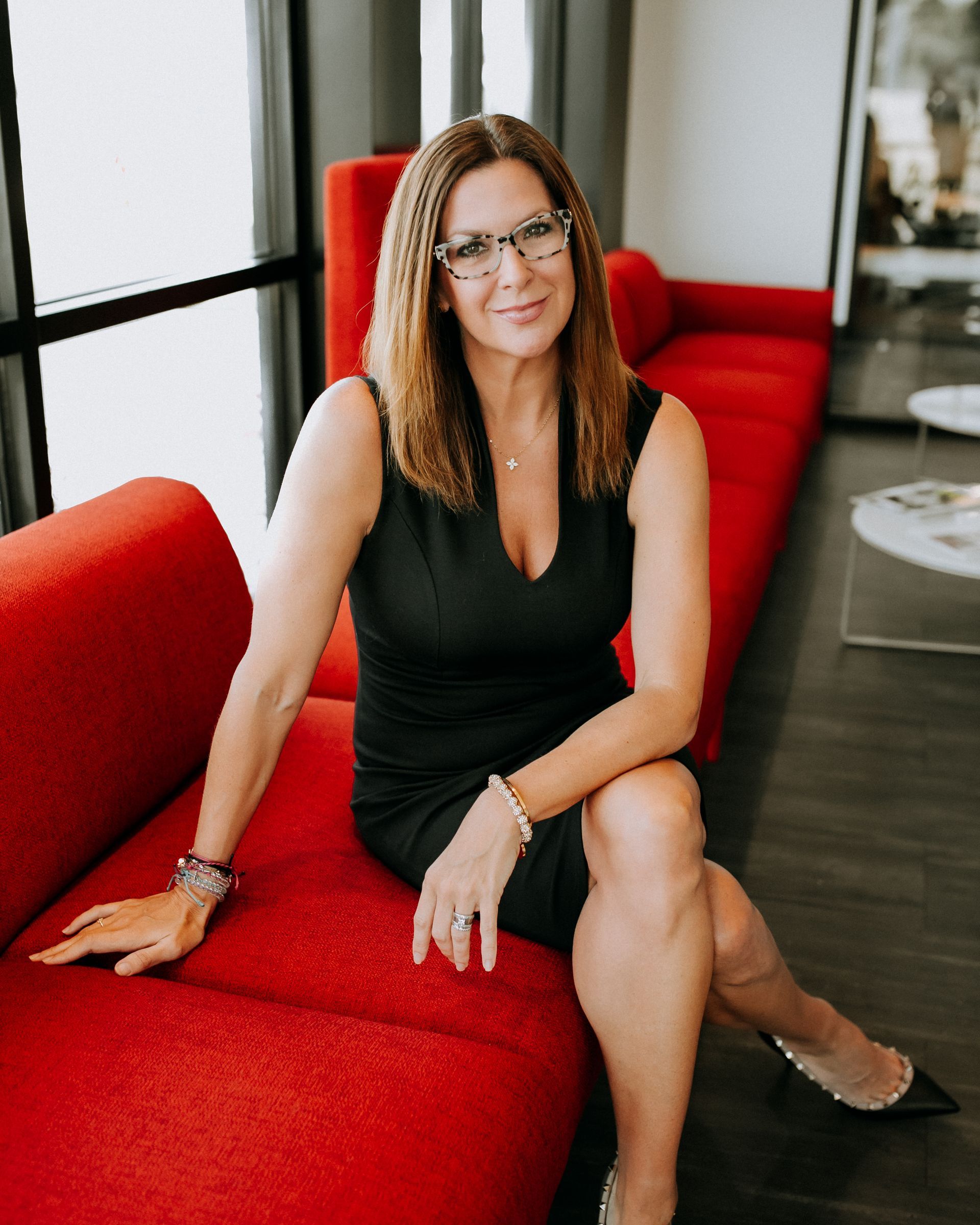 Woman in black dress sitting on a bright red couch in a modern room, smiling at the camera.