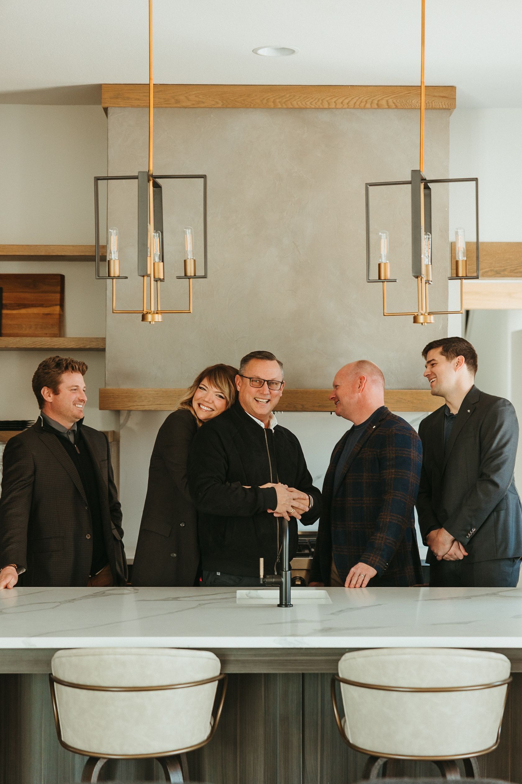 Five men in suits talking in a modern room with pendant lights and a bar counter