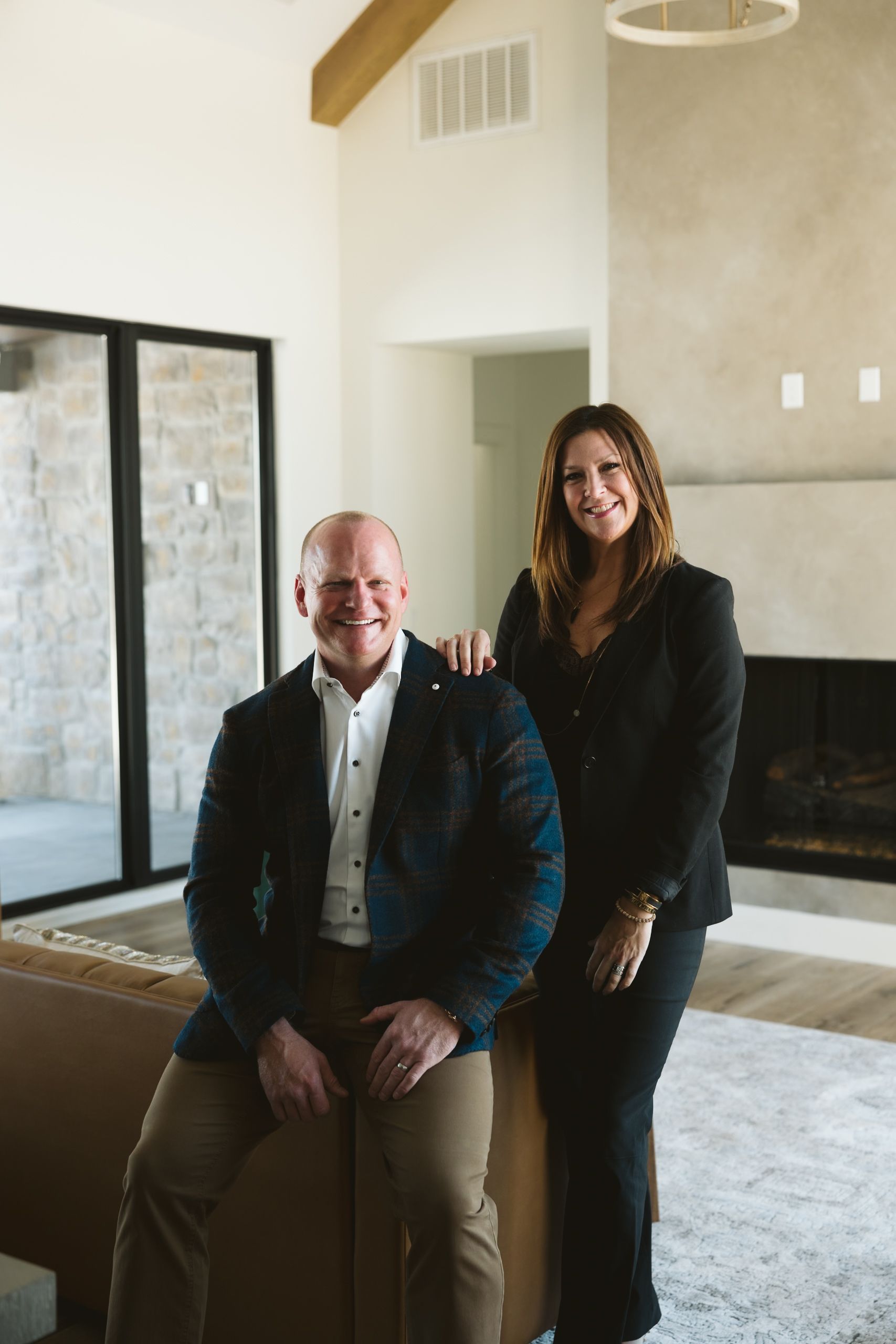 Two people posing in a modern living room with a fireplace and large windows