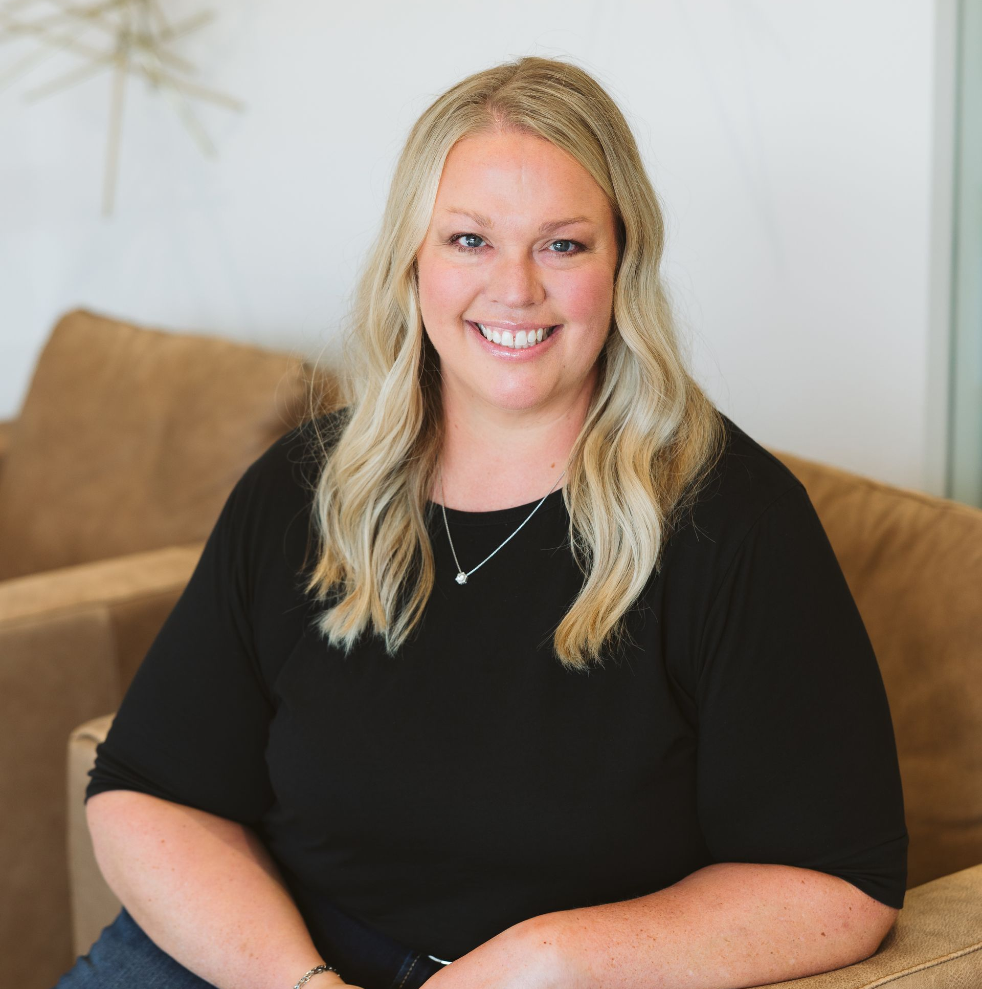 Smiling woman with blonde hair in a black top seated on a tan couch
